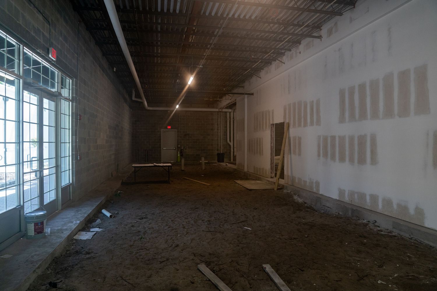 Unfinished commercial space showing exposed ceiling, drywall, and large windows during renovation.