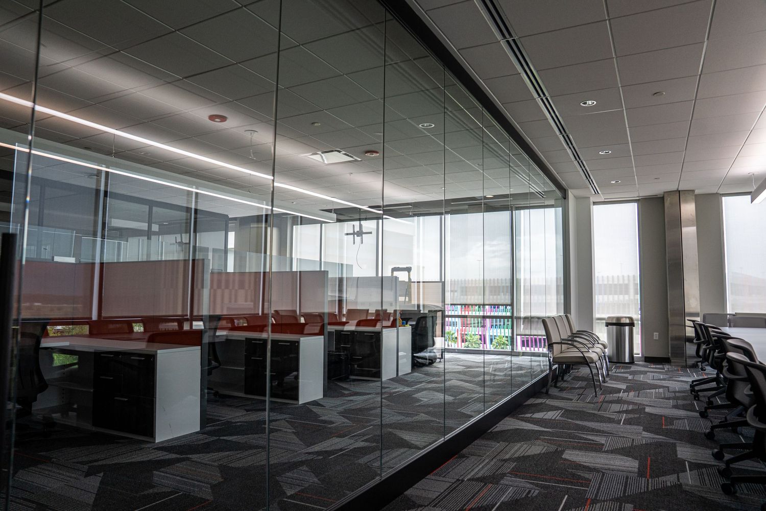 Panoramic view of an empty modern office space with glass walls and carpeted flooring.