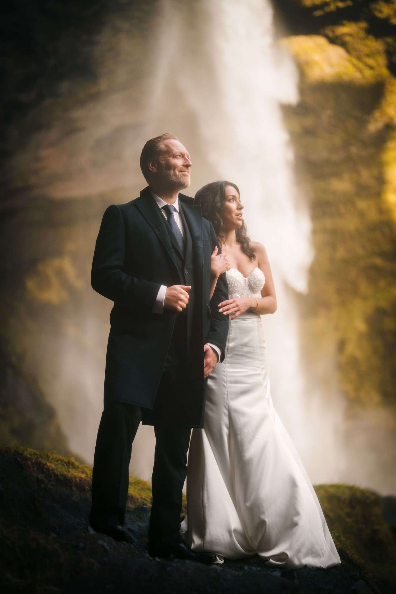 Iceland destination wedding. Wedding party poses against dramatic waterfall backdrop in formal attire.