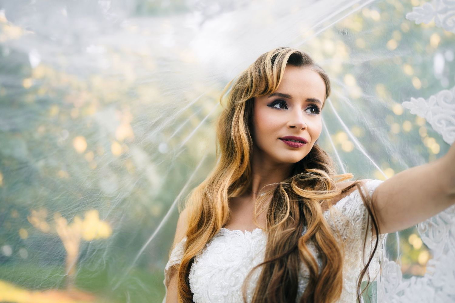 Mississauga bridal portrait in a white dress smiles while taking a selfie outdoors with sunlit bokeh in the background.