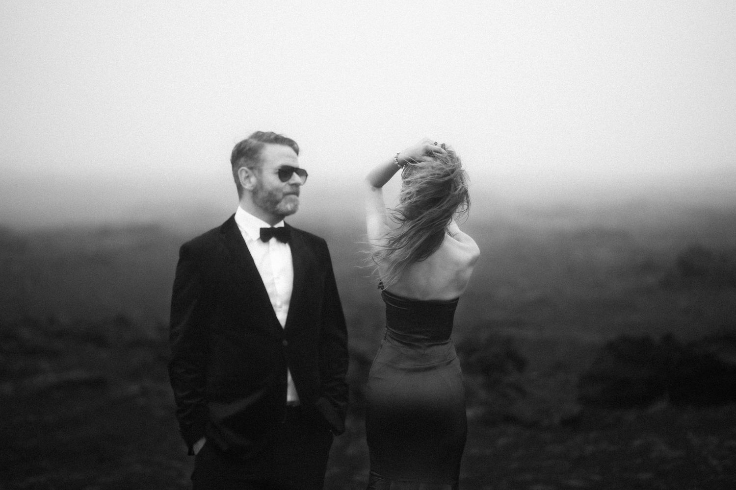 Iceland destination wedding. A black and white wedding photo showing intimate moments between a couple in formal attire on a misty hillside.