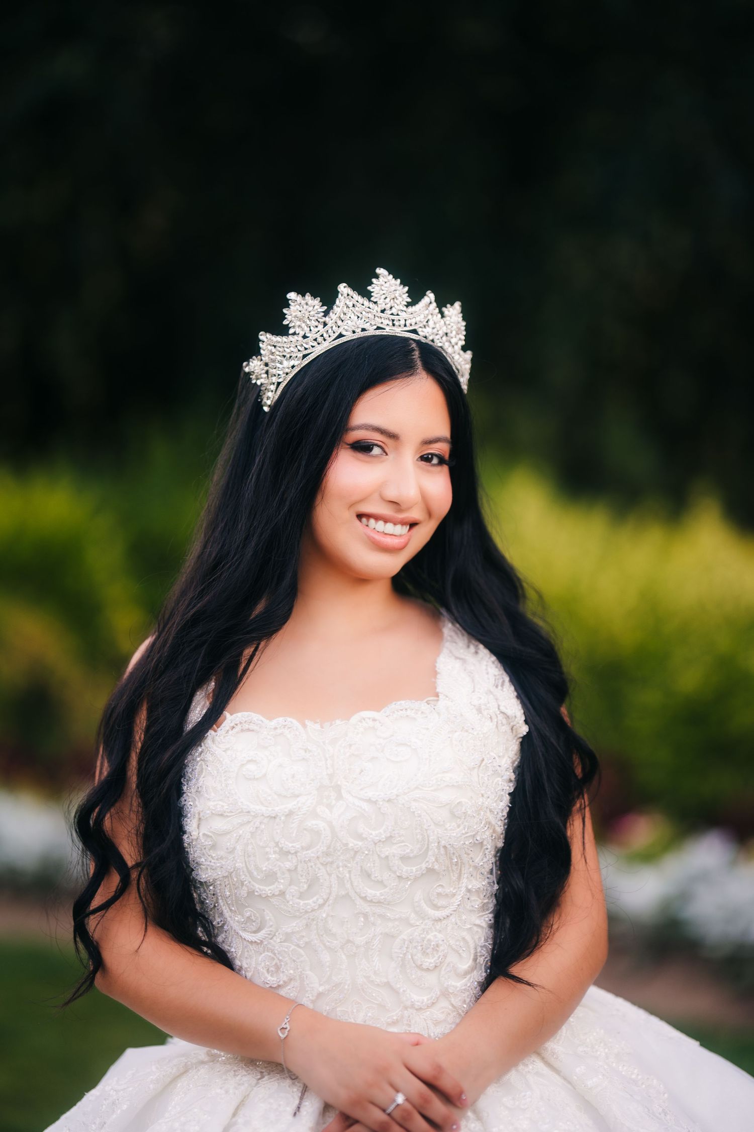 Bride in white lace wedding dress with long dark hair poses outdoors during golden hour photoshoot.