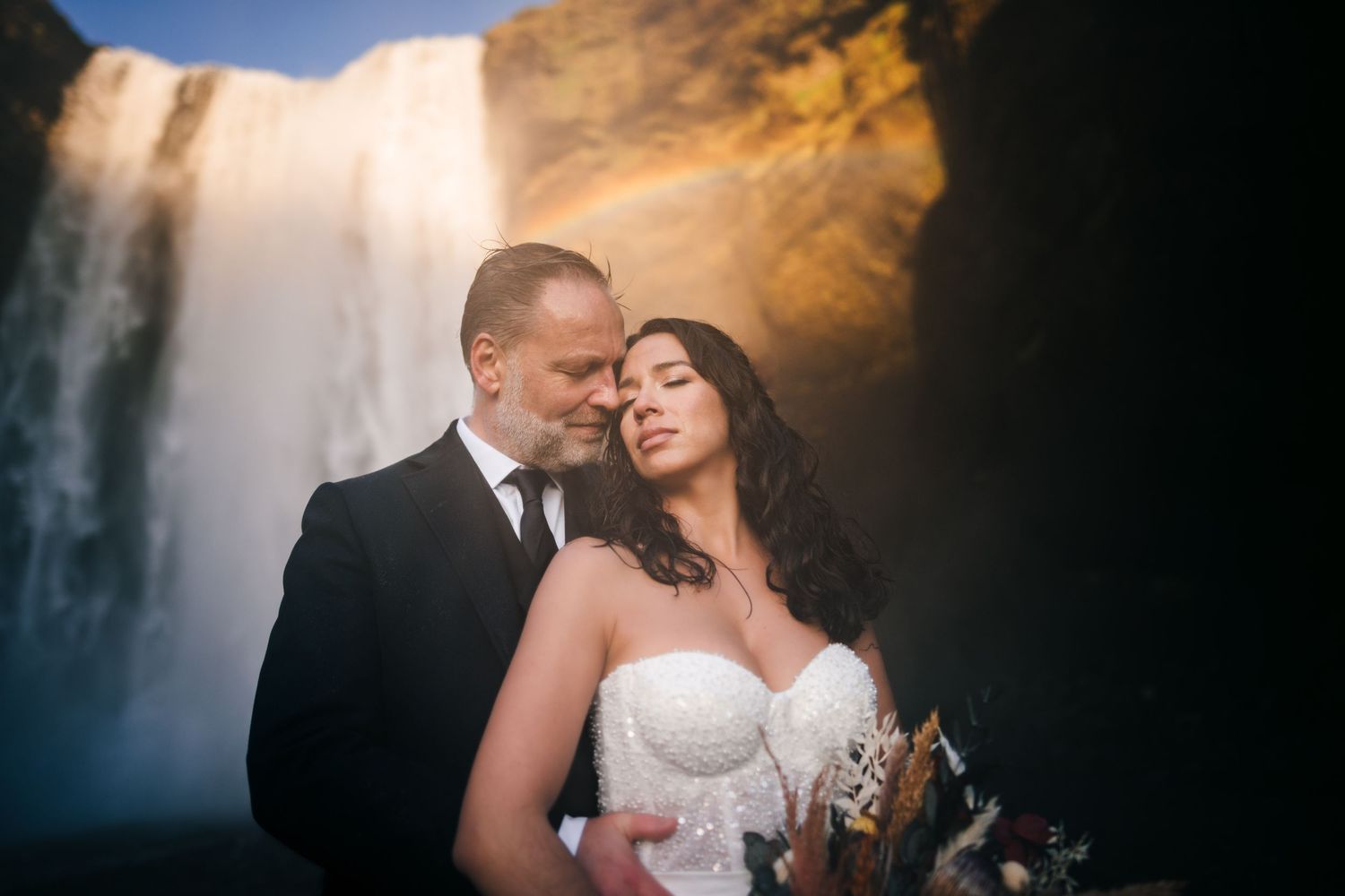 Iceland destination wedding. Romantic wedding couple embraces in front of dramatic waterfall during sunset photo session.
