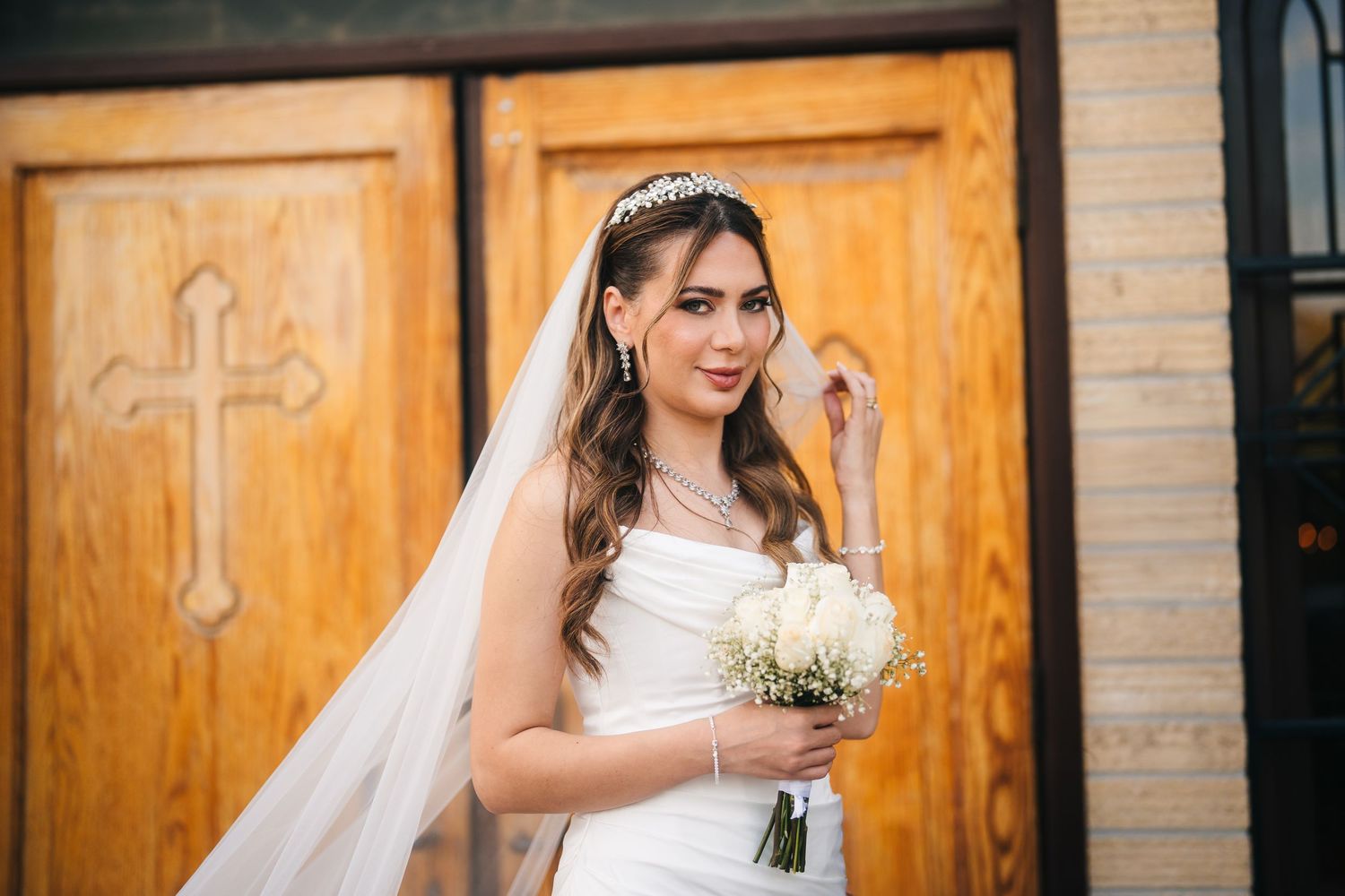 Markham Orthodox Church Bride in white wedding dress holds bouquet while standing in front of wooden church doors with crosses.