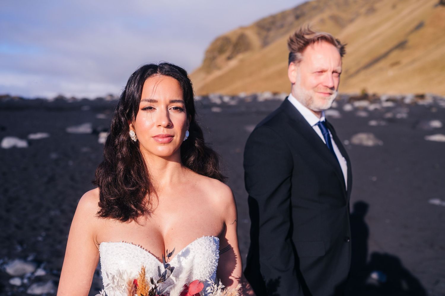 Iceland destination wedding couple poses together on a scenic beach for their wedding photos with mountains and ocean in the background.