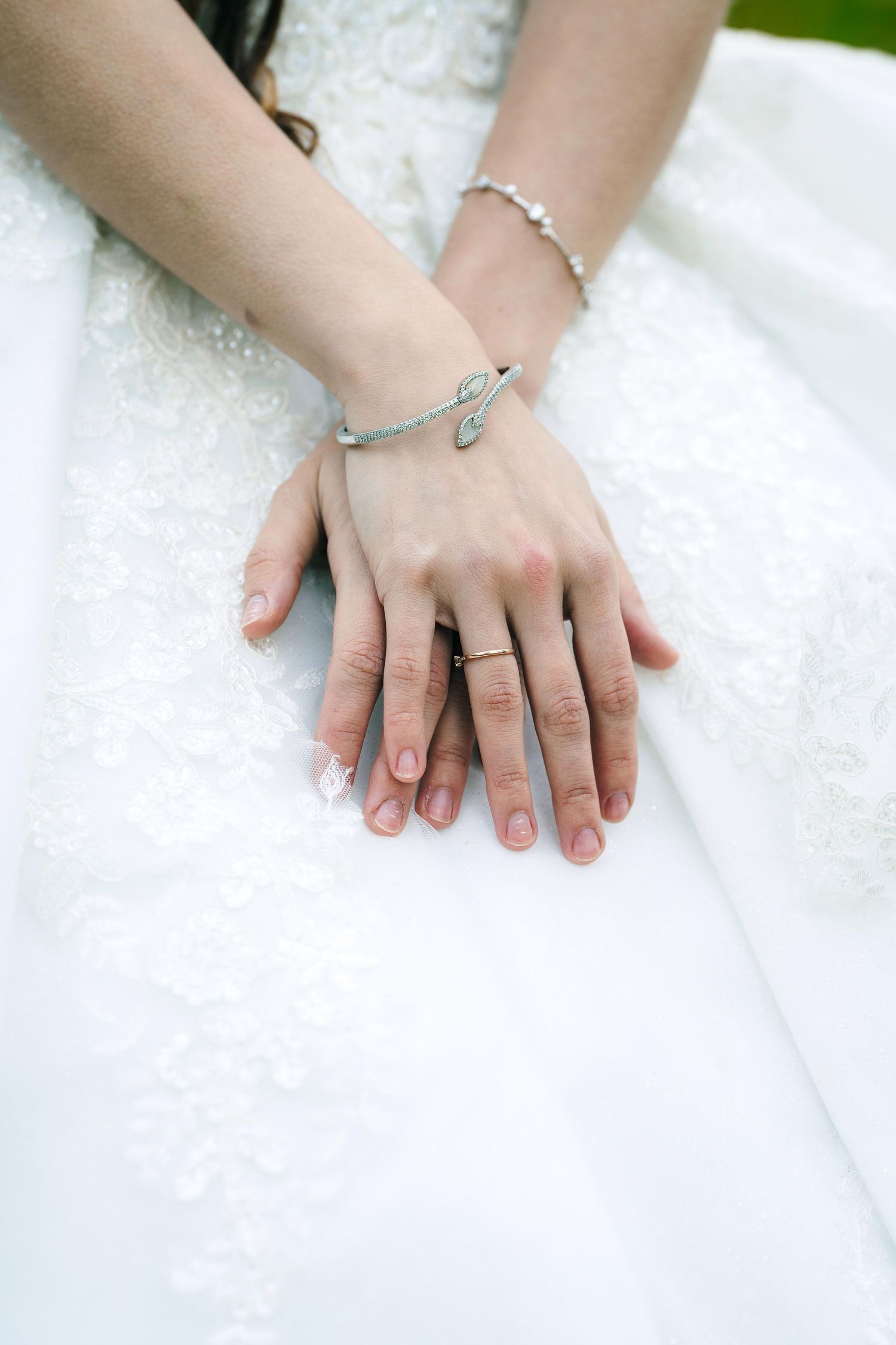 Mississauga bridal portrait. Close-up view of hands wearing delicate silver jewelry and rings against a white lace background.