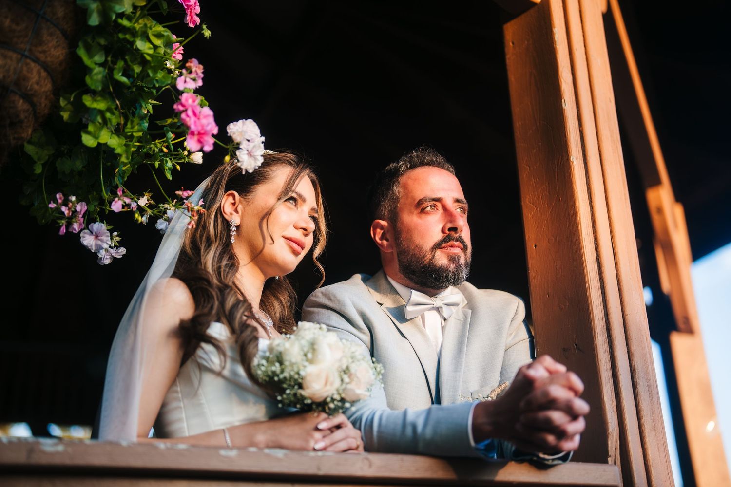 A couple shares joyful laughter during an outdoor wedding celebration near wooden pillars and pink flowers.