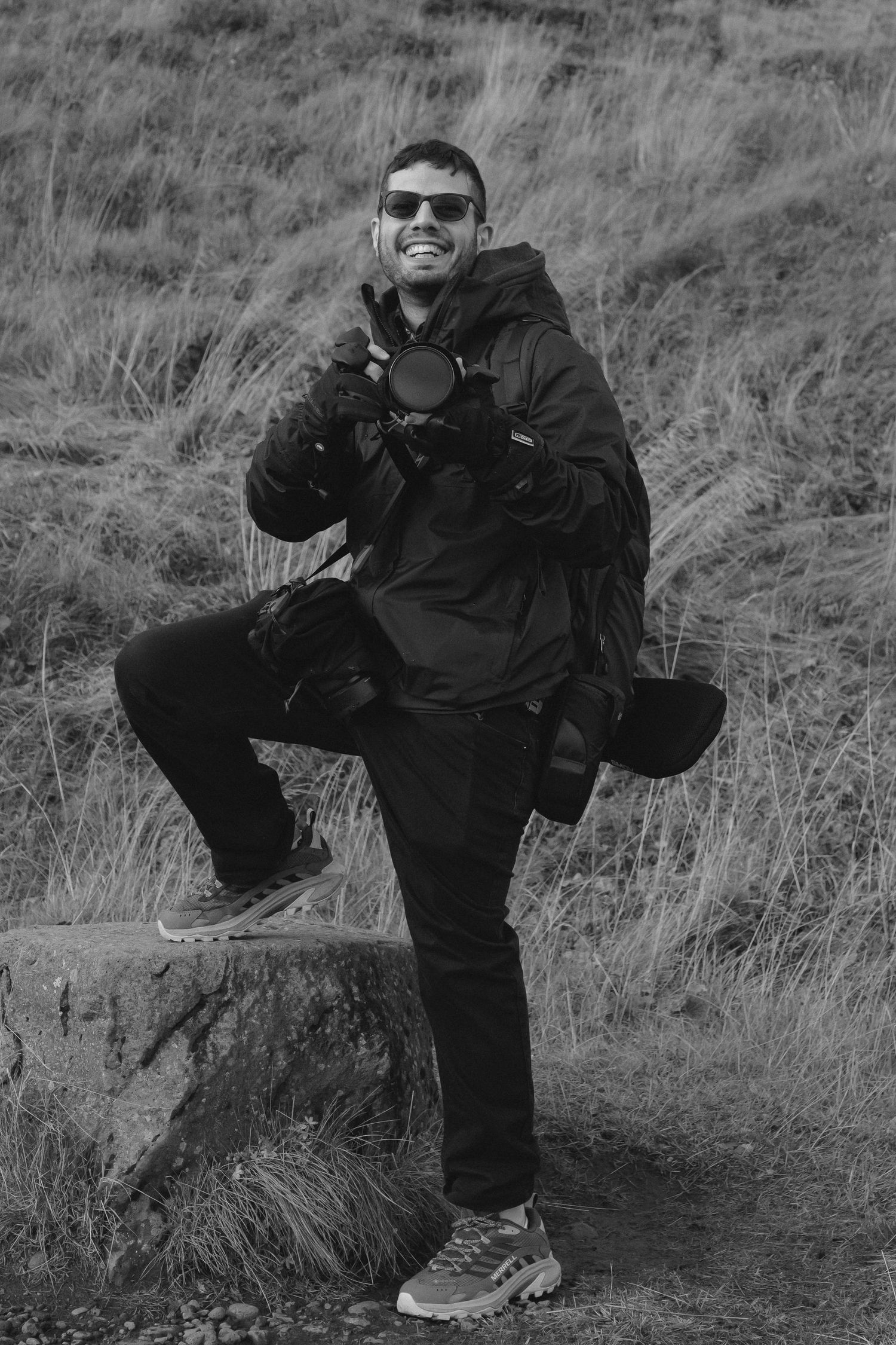 Gildedweddings.ca photographer. A hiker in sunglasses and dark outdoor gear poses on a rocky hillside in black and white photography.