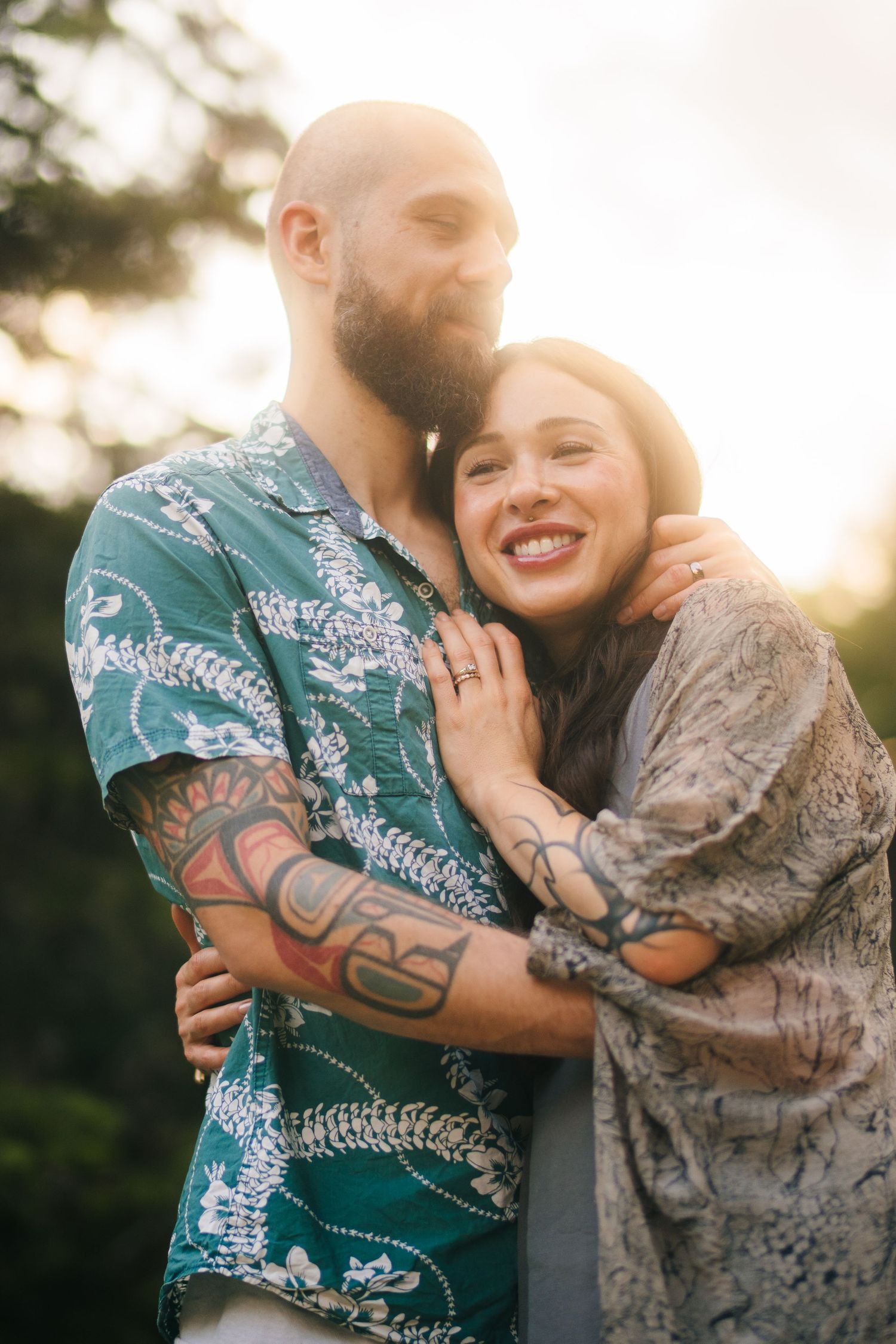 A couple in a Hawaiian shirt and lace dress embrace lovingly during a golden sunset photoshoot outdoors.