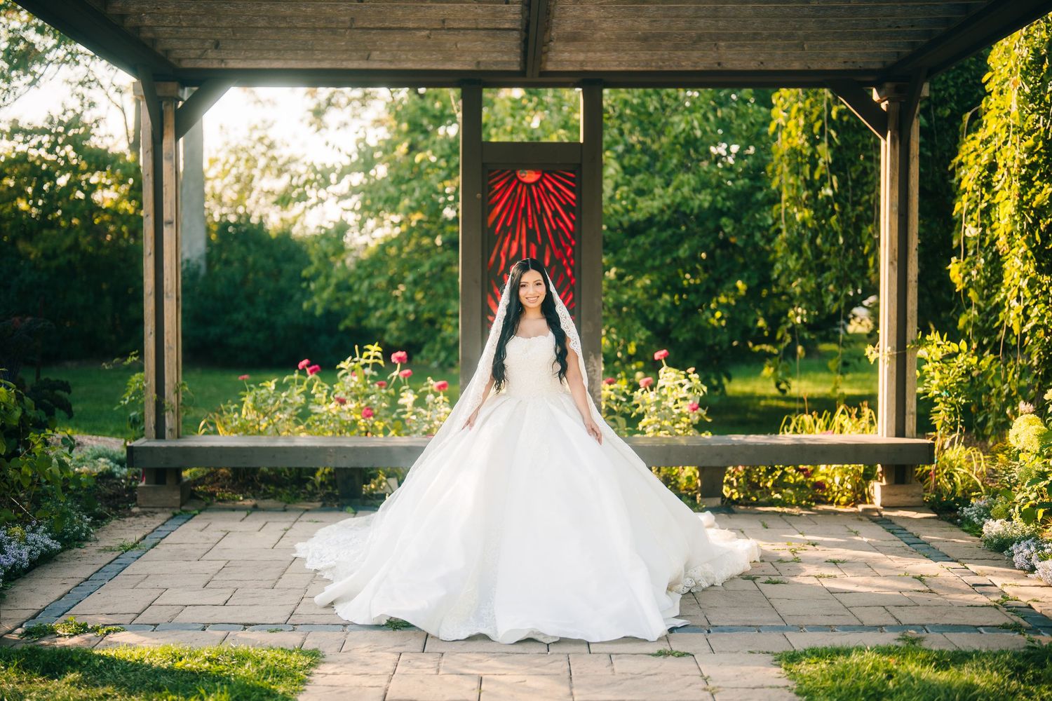 Oakville Bridal portrait. A bride in a flowing white wedding gown stands in a scenic outdoor gazebo surrounded by lush greenery.