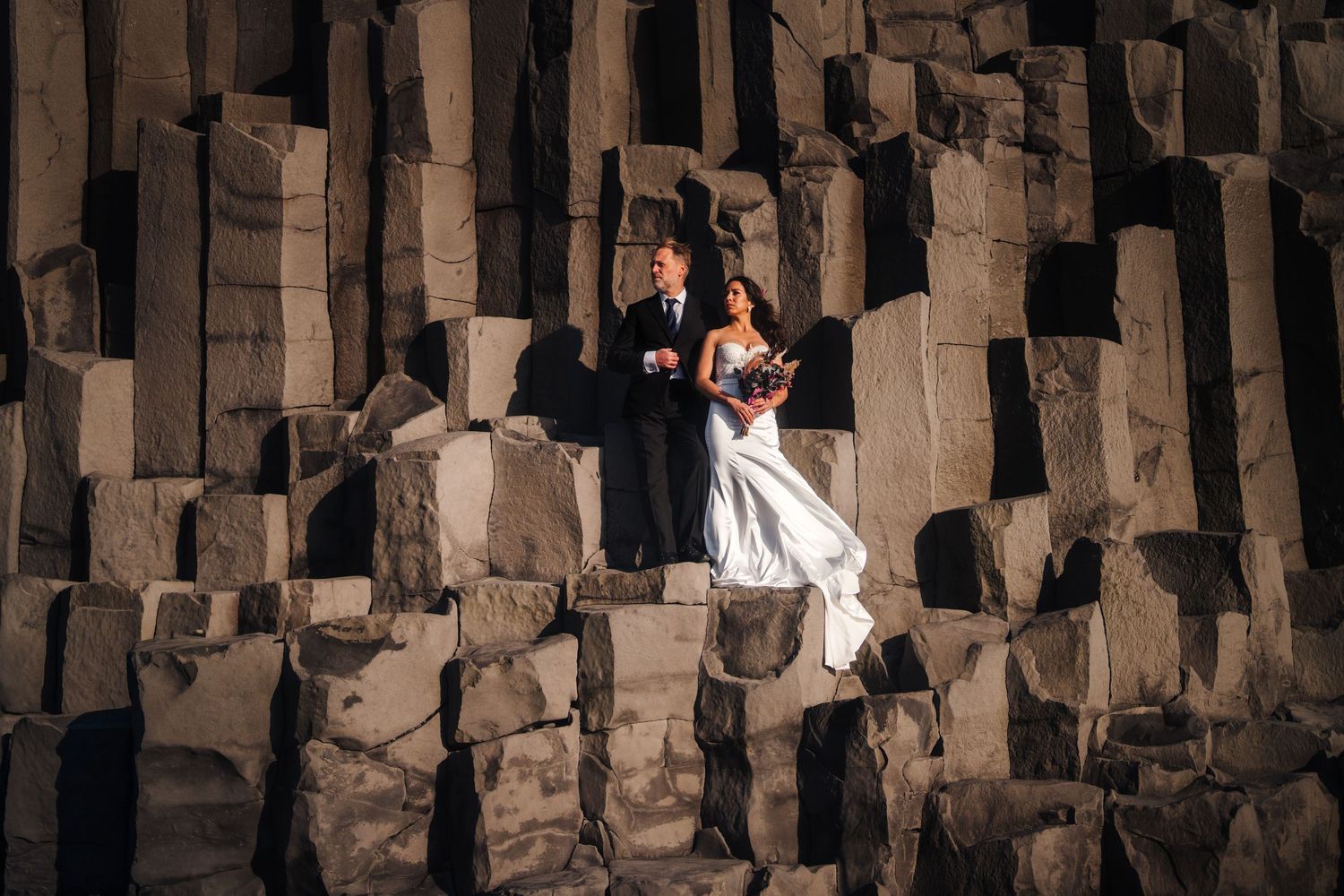 Iceland destination wedding couple poses against dramatic basalt columns at Giant's Causeway in Northern Ireland at sunset.