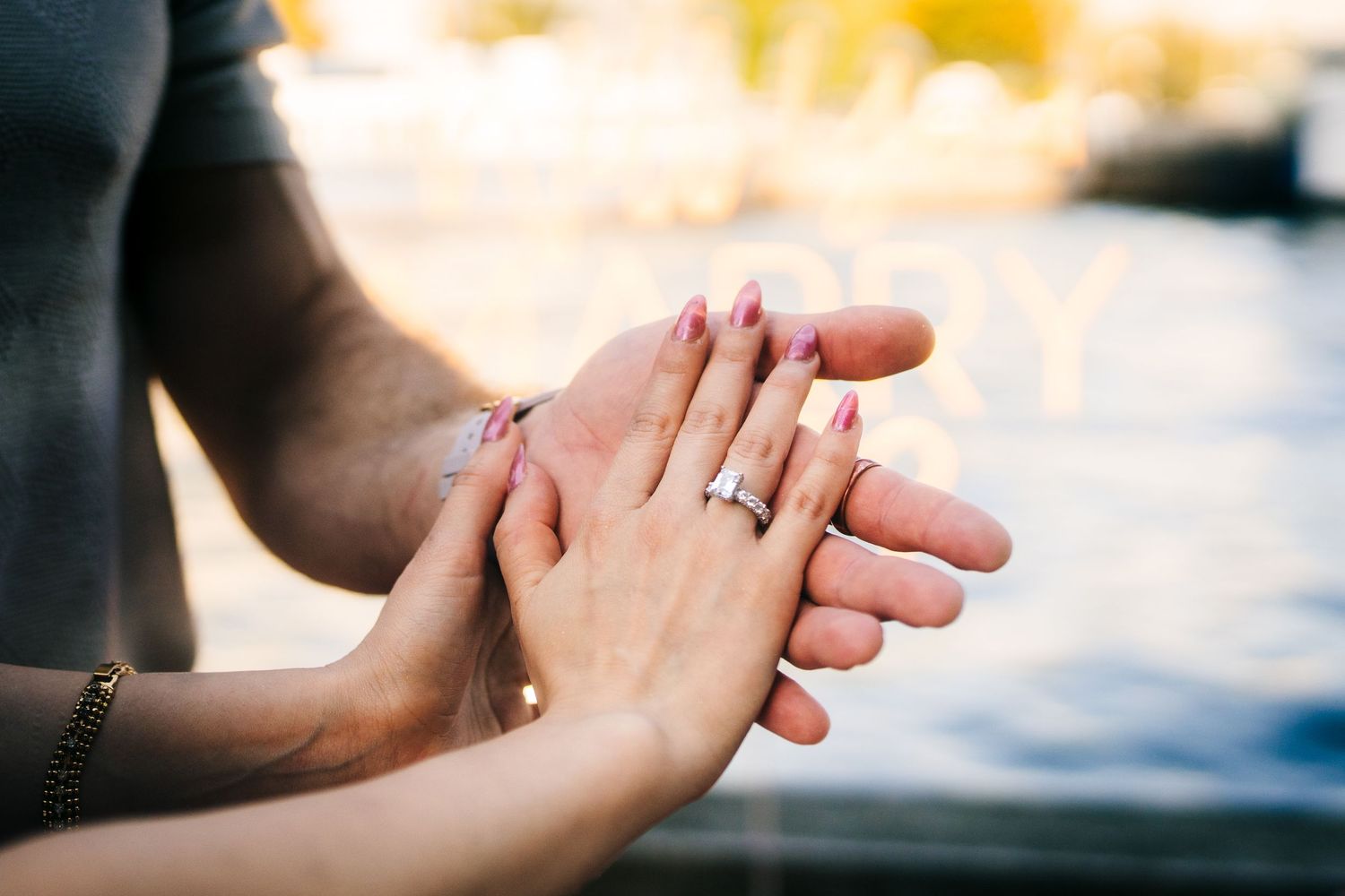 Close up of hands holding each other tenderly with an engagement ring visible in soft natural lighting.