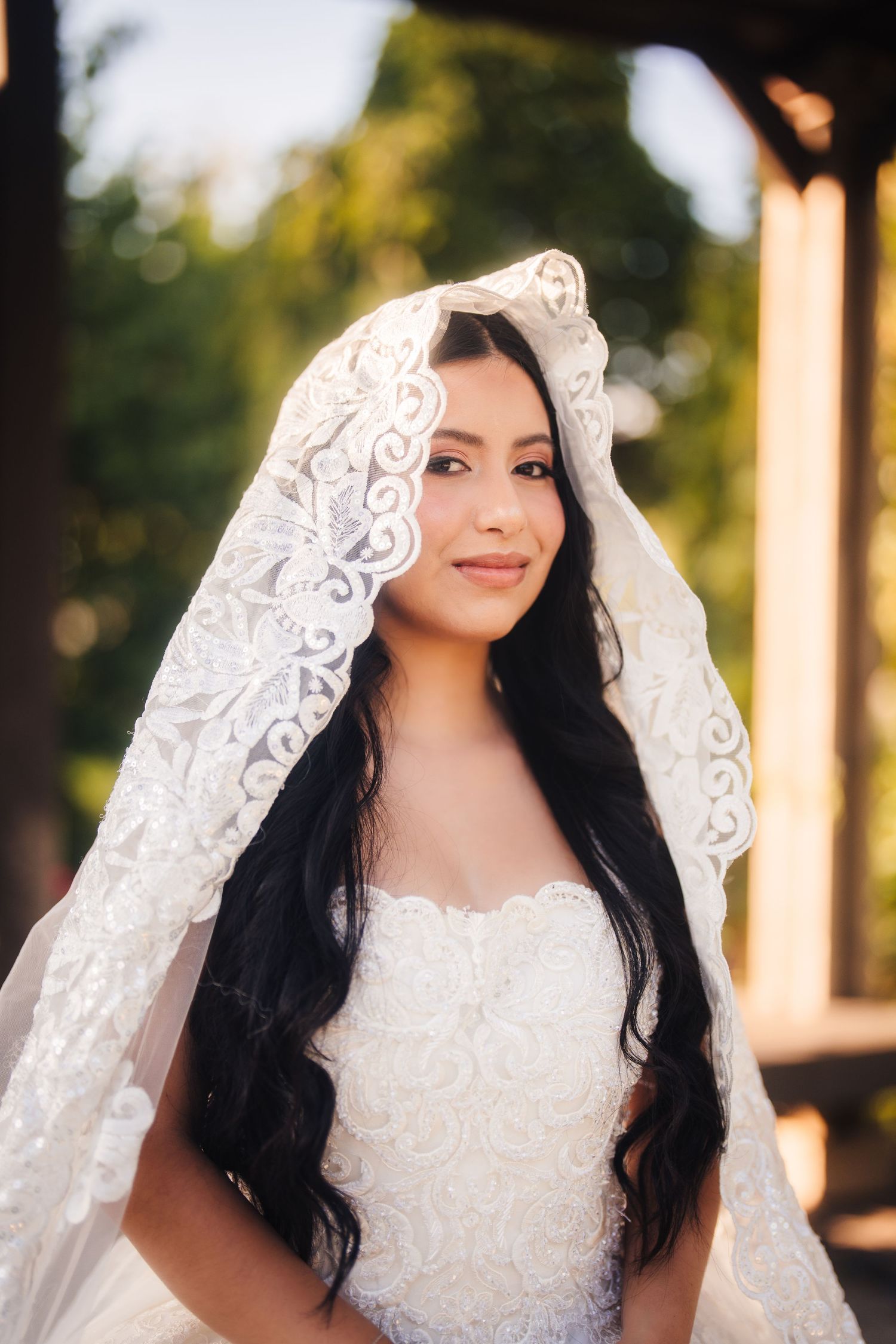 Oakville bride wearing a delicate white lace veil and wedding dress with long dark hair poses outdoors at sunset.