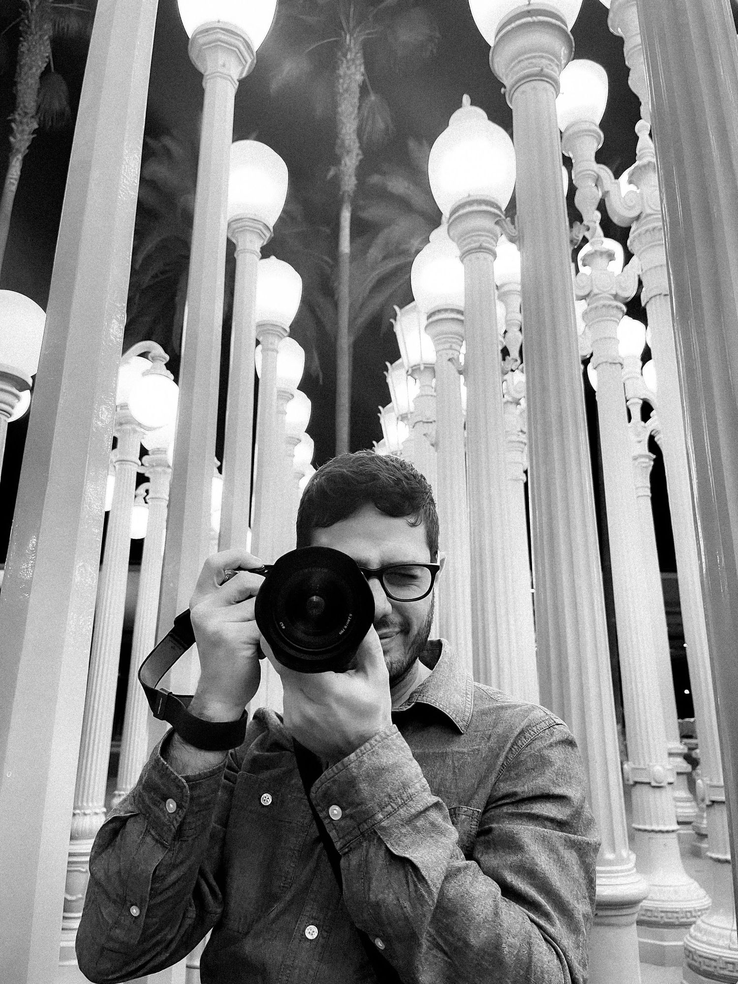 Three people take photos through white architectural columns in a mirrored artistic composition.