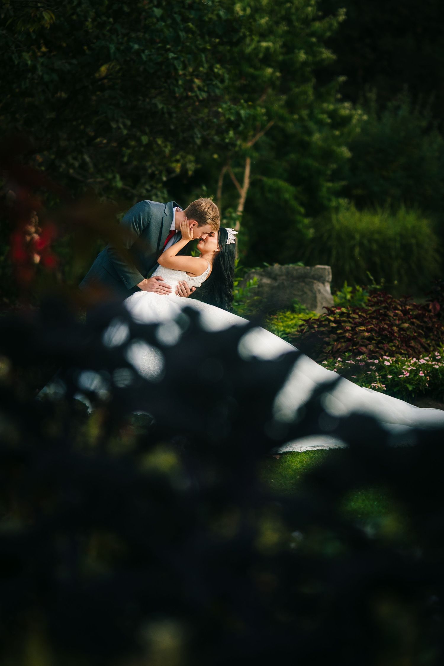 Oakville romantic couple shares an intimate moment in a garden setting with dappled sunlight filtering through the trees.