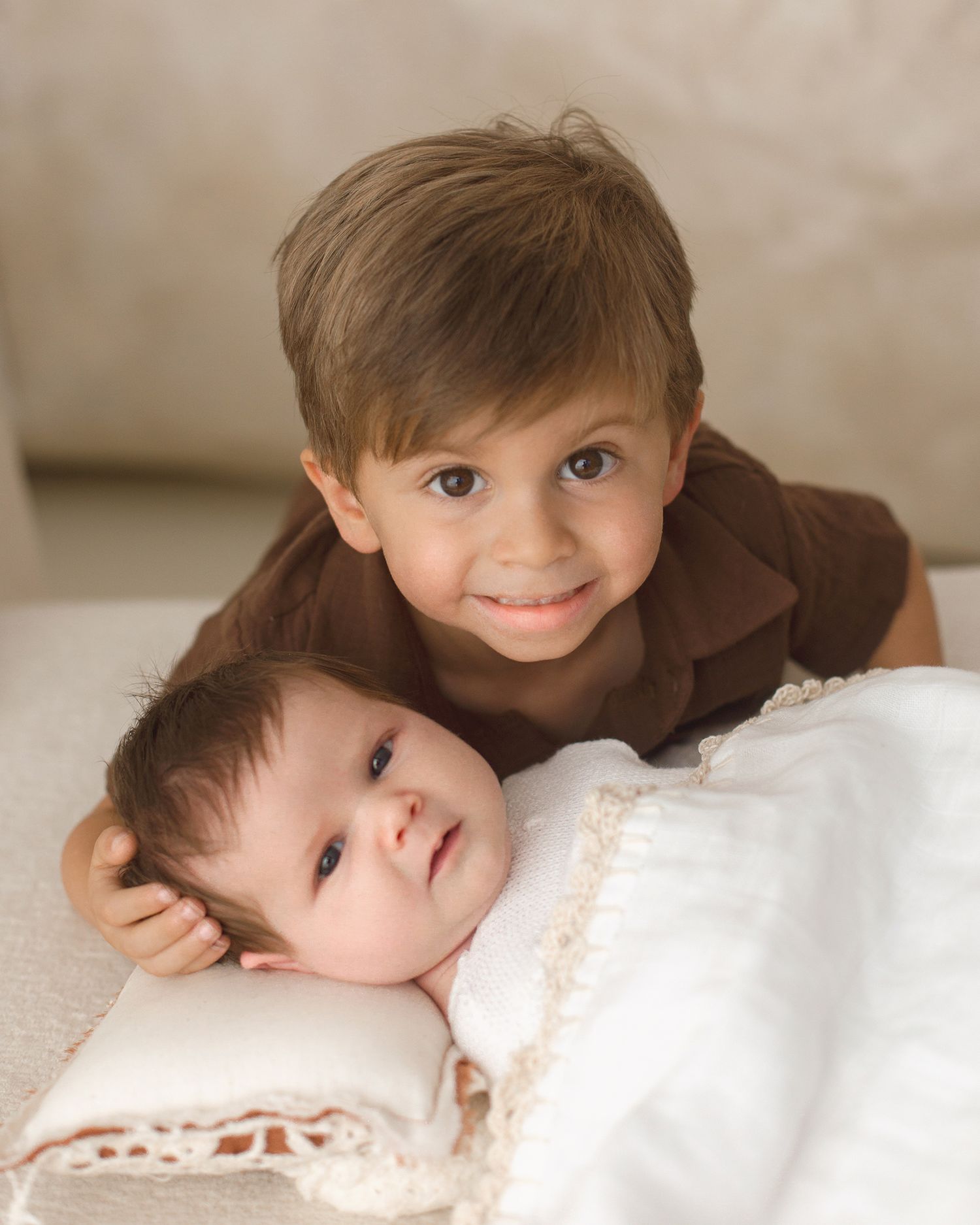 Smiling toddler boy resting chin on newborn sibling