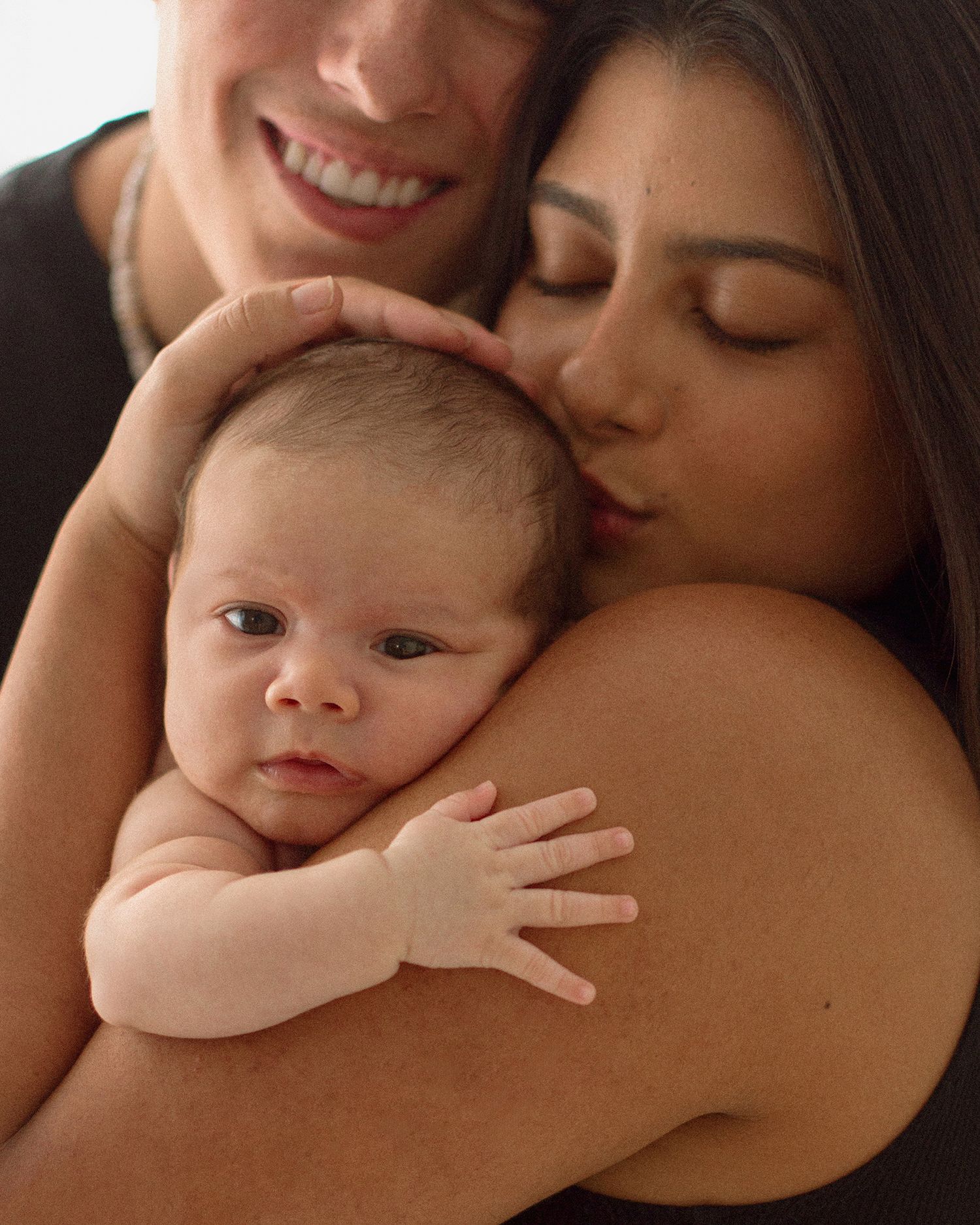 Two women lovingly hold and kiss a newborn baby, sharing a tender family moment together.