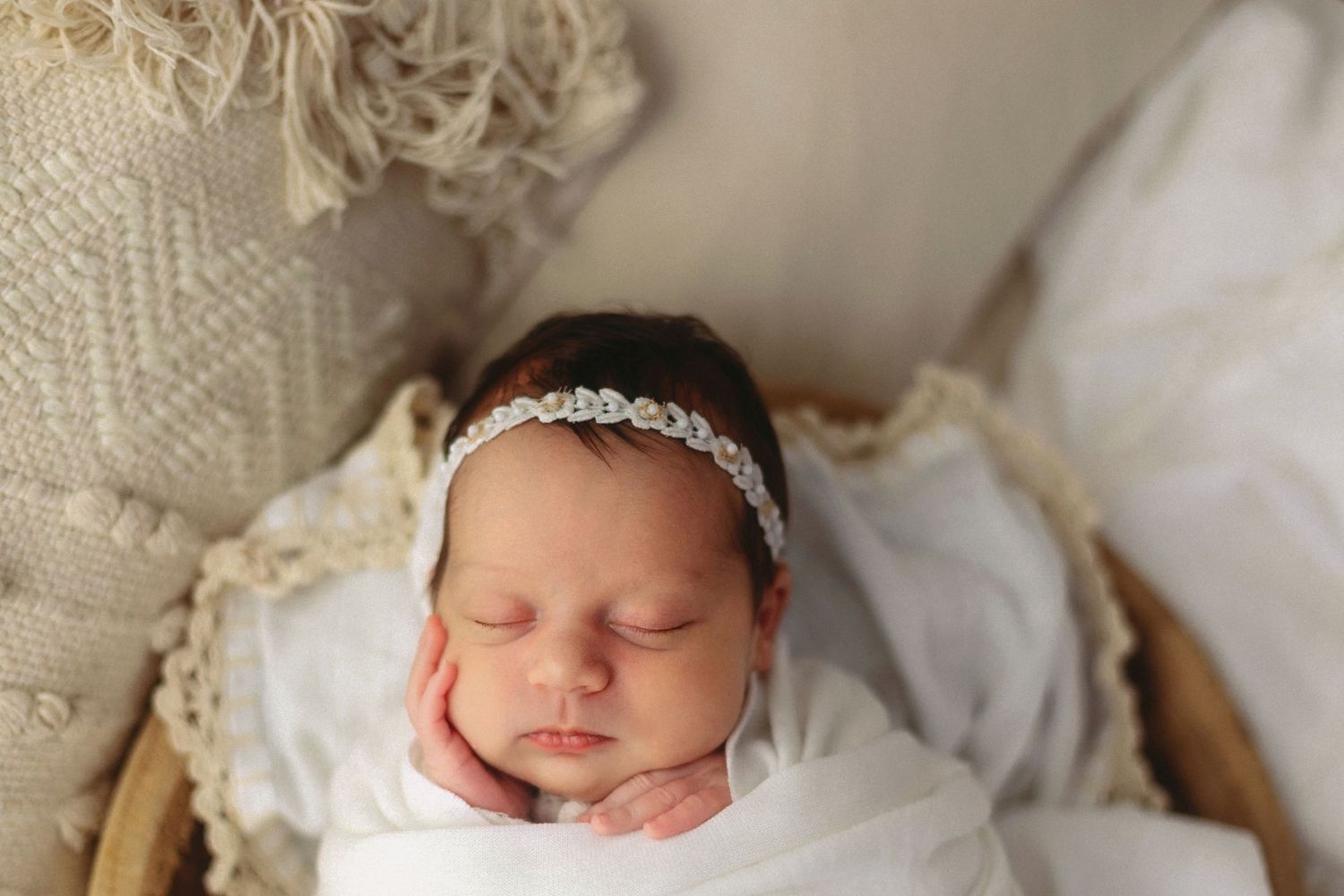 Peaceful newborn baby girl sleeping swaddled in white wrap with delicate rhinestone headband in cozy basket.
