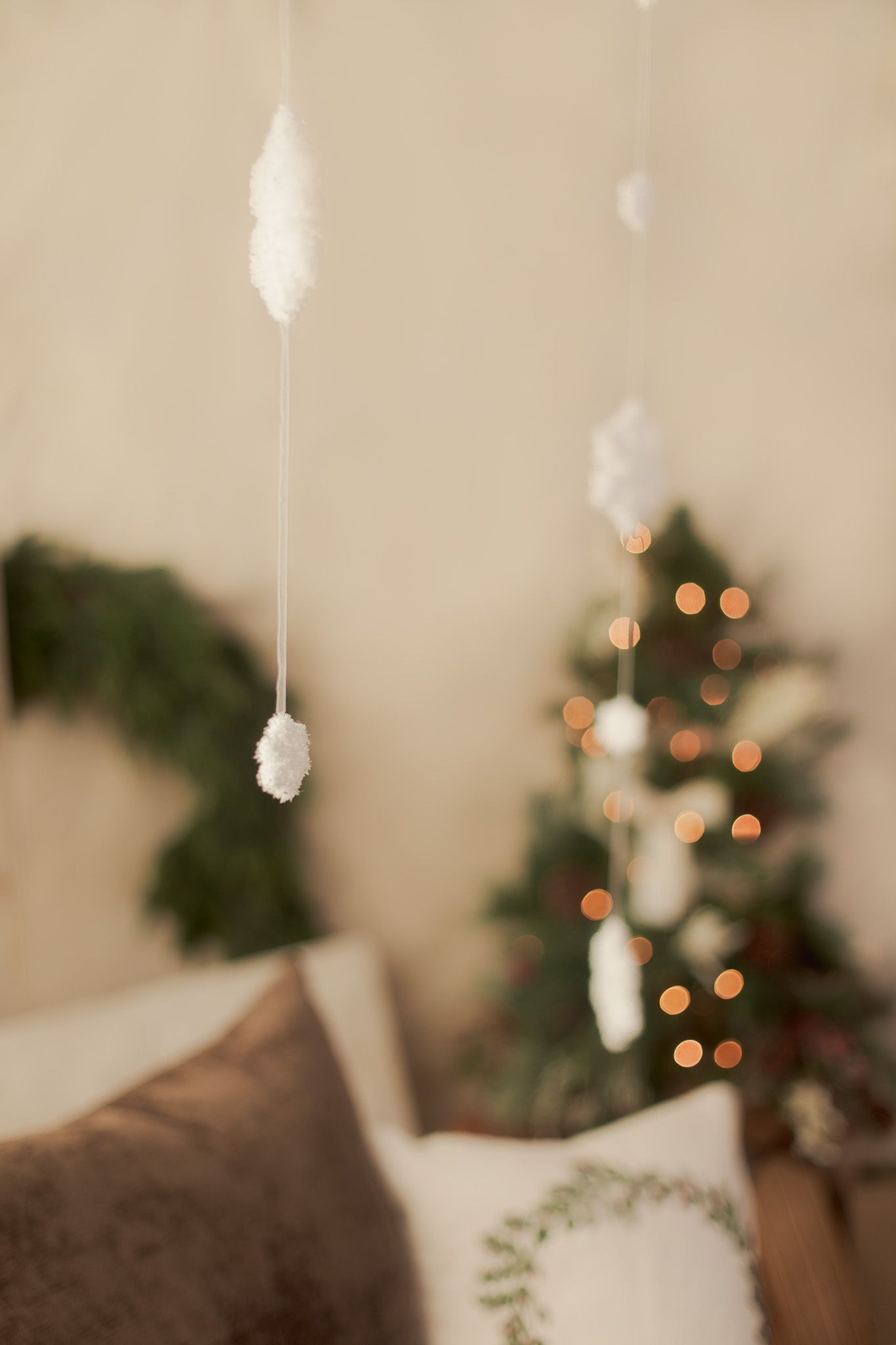 Cozy Christmas bedroom with white feather ornaments, glowing tree lights, green wreath, and decorative pillows in neutral tones.