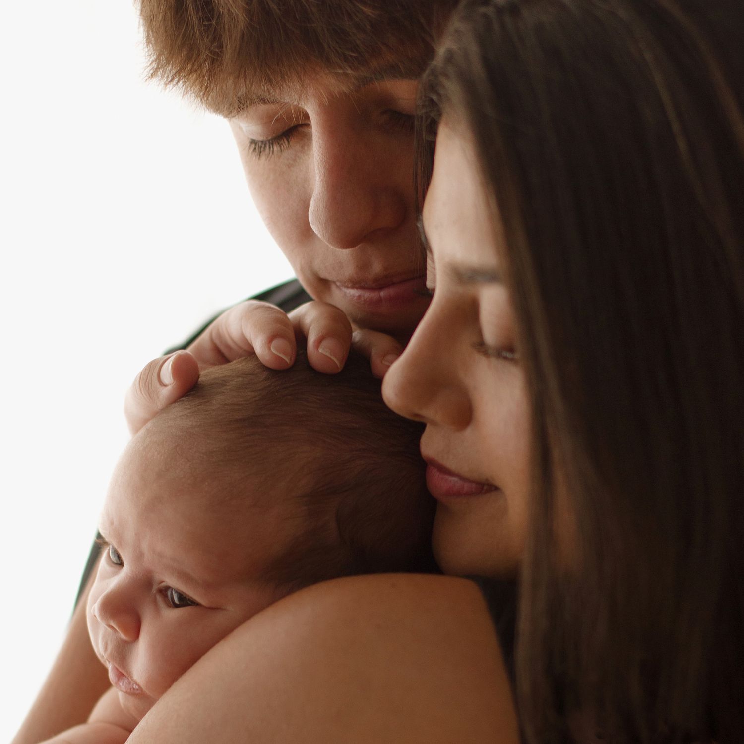 Two parents tenderly cradling their newborn baby, sharing an intimate family moment.
