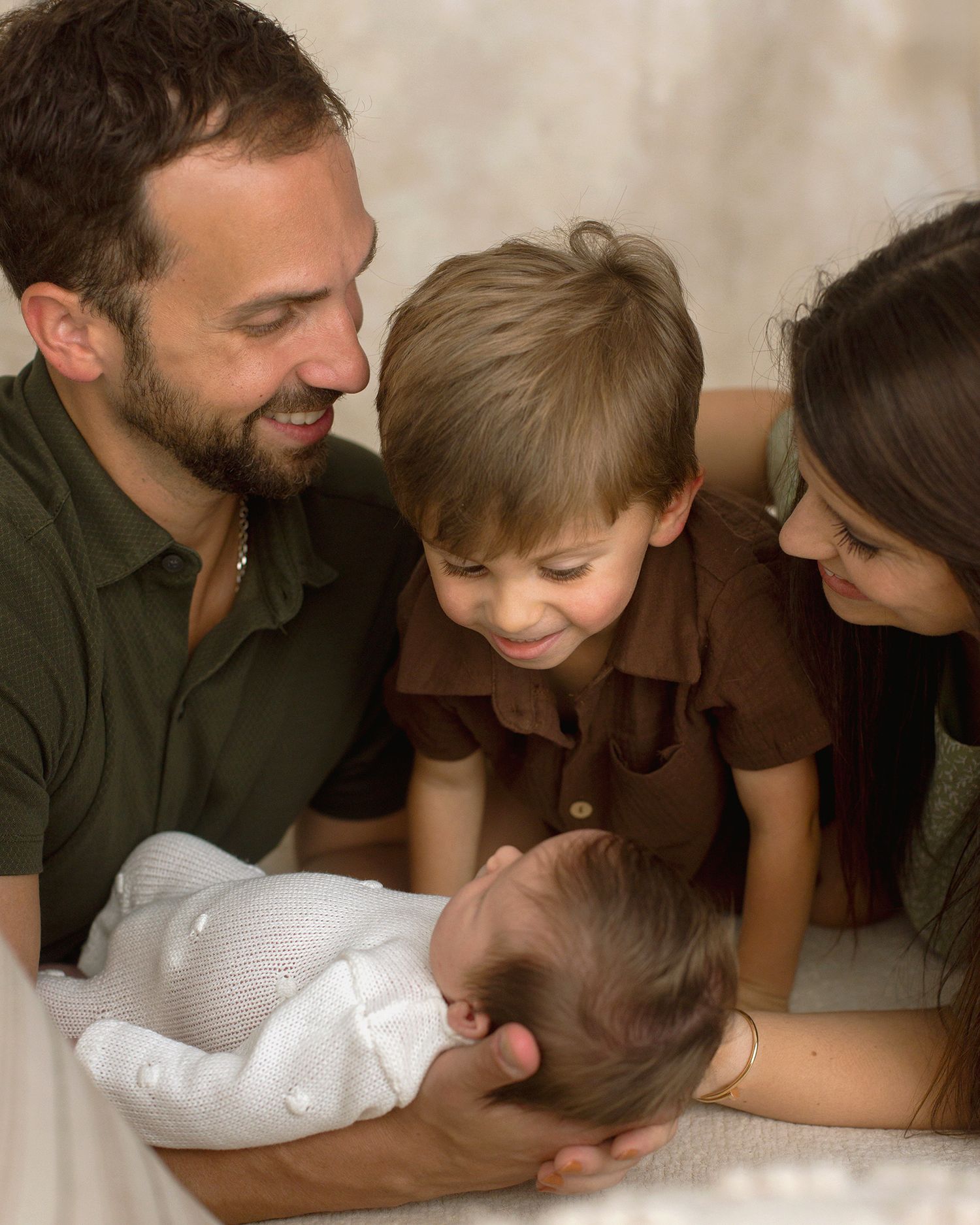 A happy family of four admires their newborn baby, with parents and young son smiling warmly together.