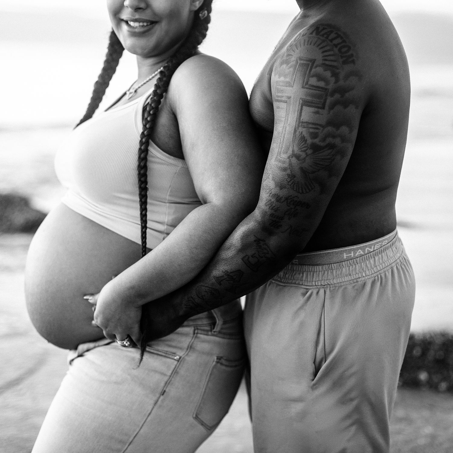 Black and white maternity photo of a pregnant woman and tattooed partner embracing on Redington Beach in Florida.