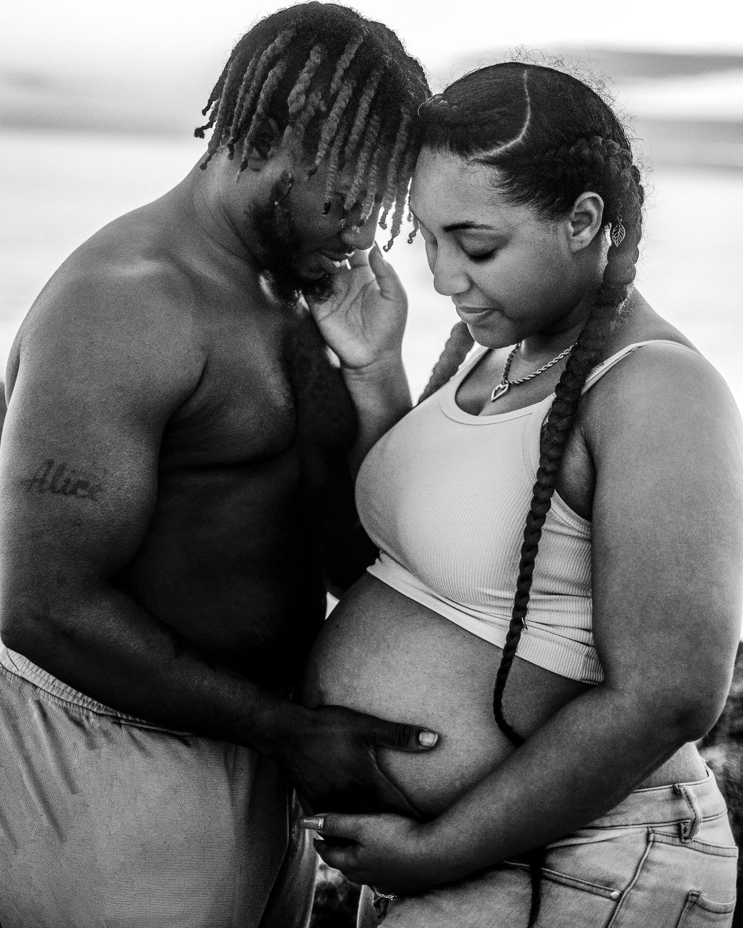 Black and white photo of couple sharing tender moment, man touching pregnant womans belly.