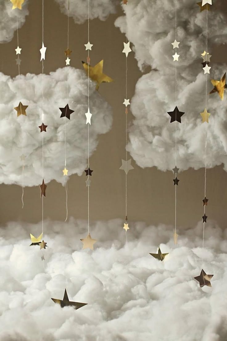 Fluffy white clouds with hanging gold and white star garlands on a warm beige background for a dreamy nursery decor.