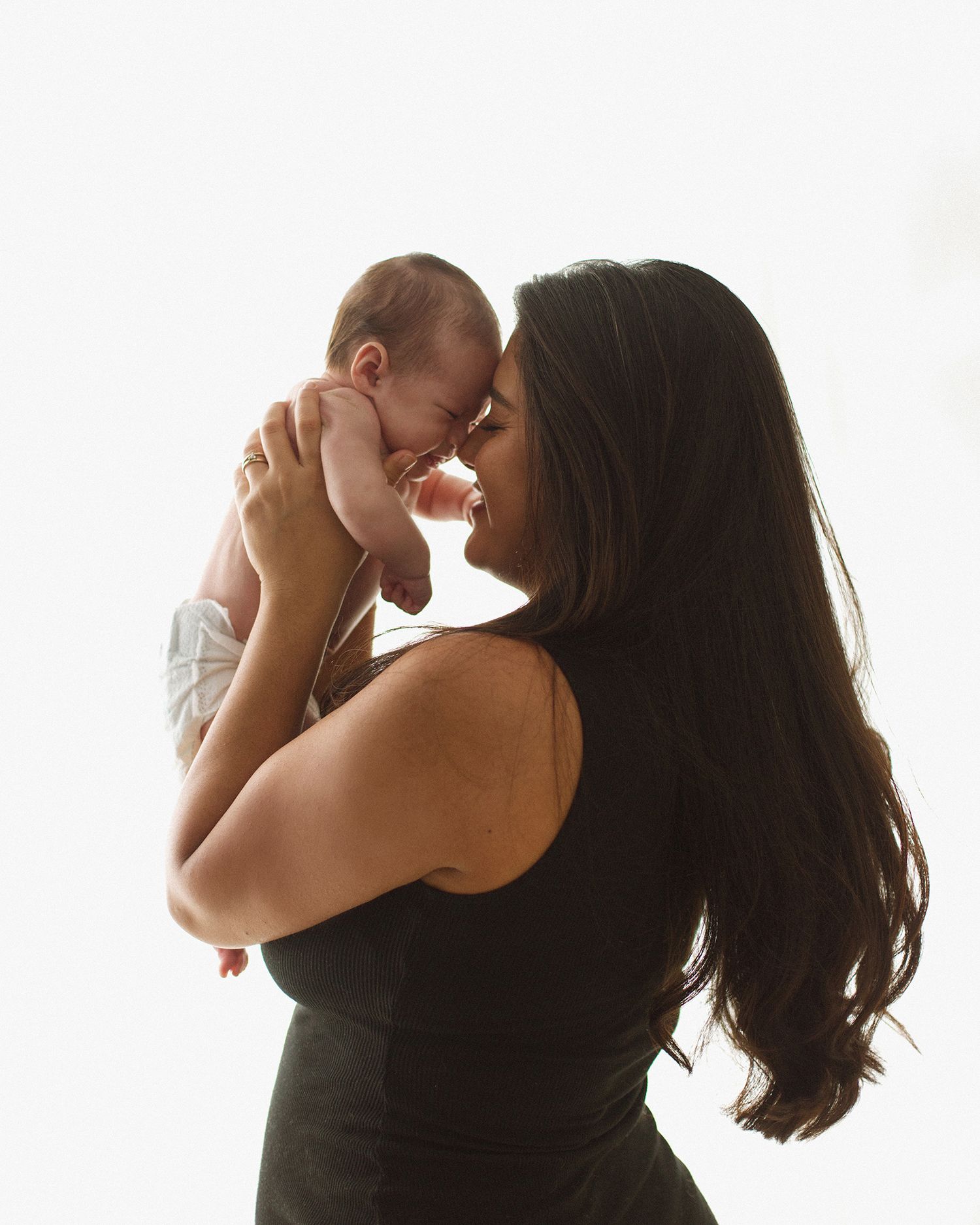 A mother tenderly holds her newborn baby close, touching foreheads in a loving embrace against a bright background.