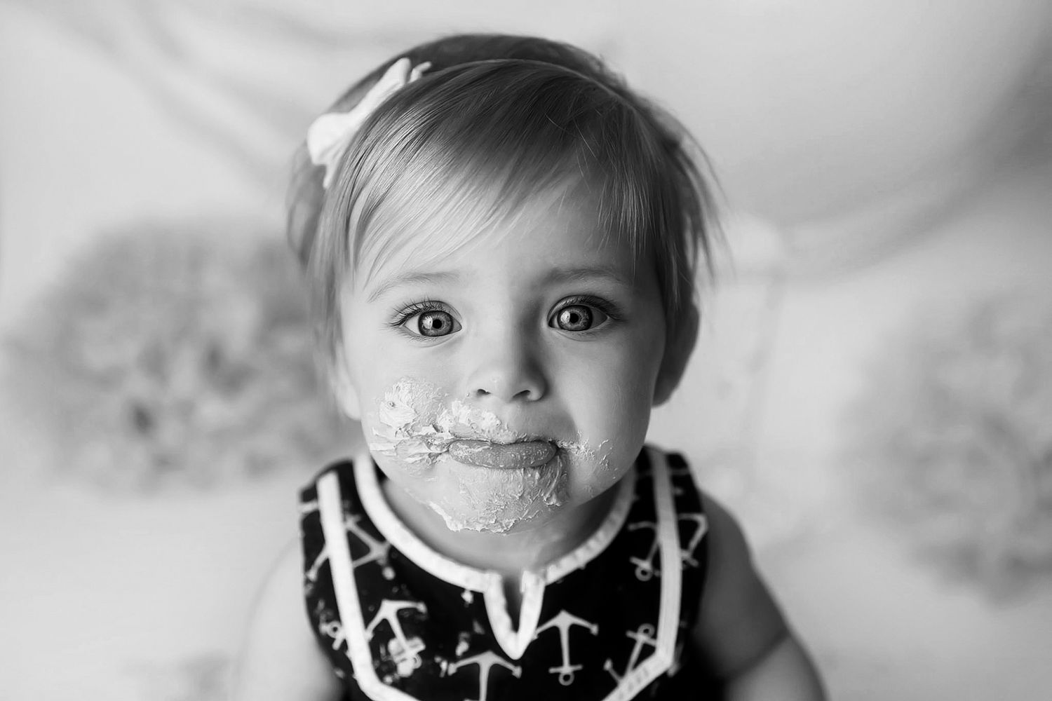 Black and white photo of a cute baby girl with cake on her face, celebrating her first birthday.