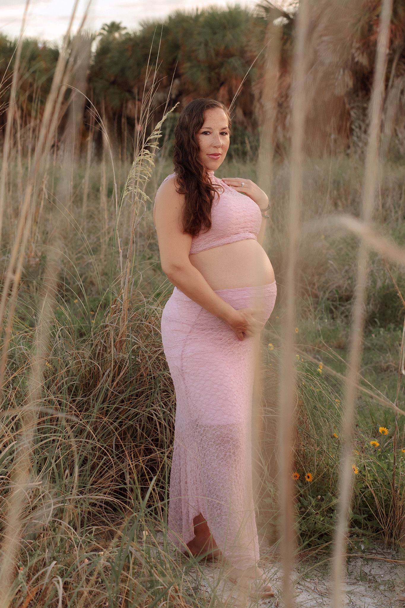 Pregnancy portraits st. Pete beach, fl amongst tall beach grass during golden hour outdoor photoshoot.