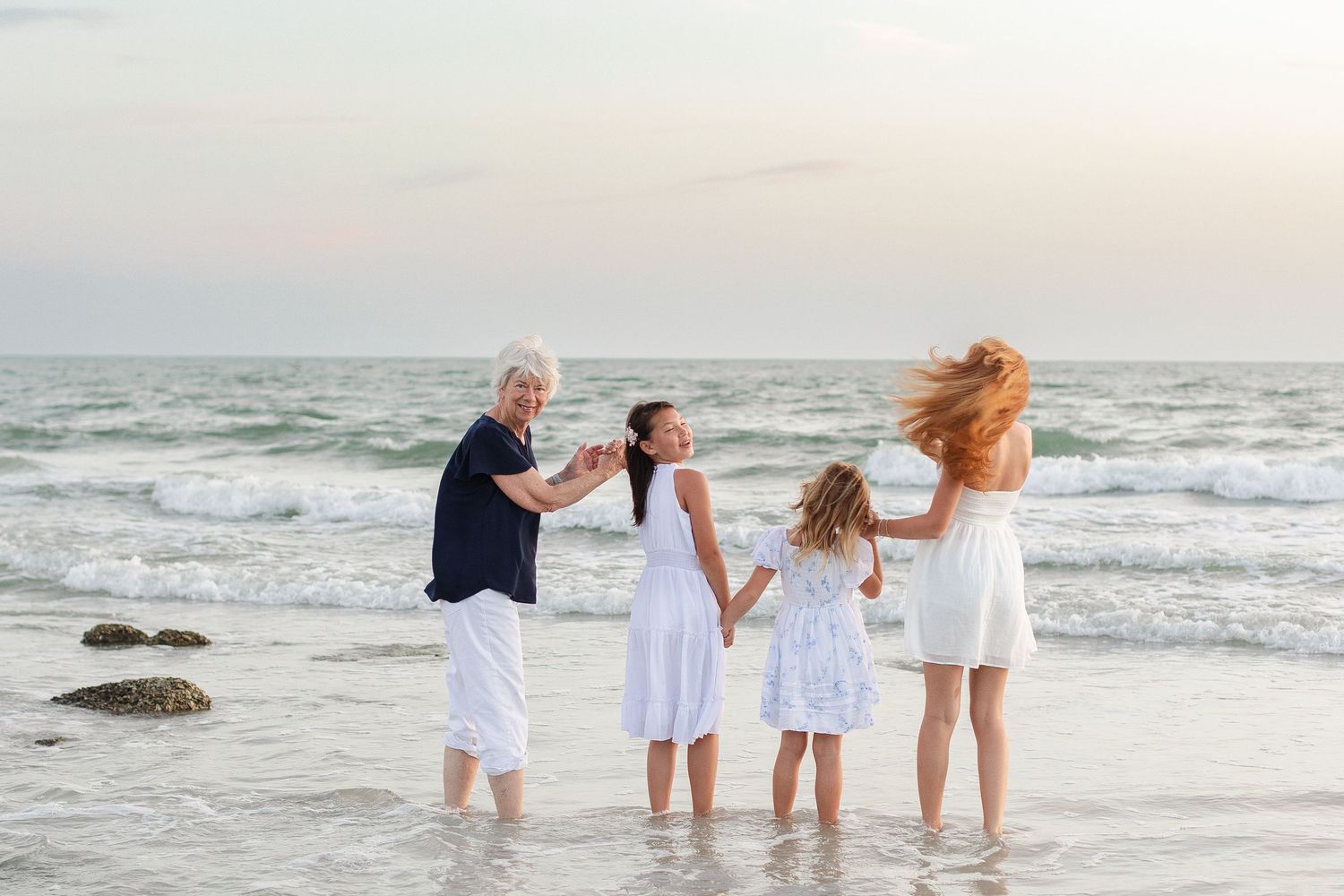 Family of four enjoying a Redington beach sunset, with grandparent and children in white dresses playing in ocean waves.