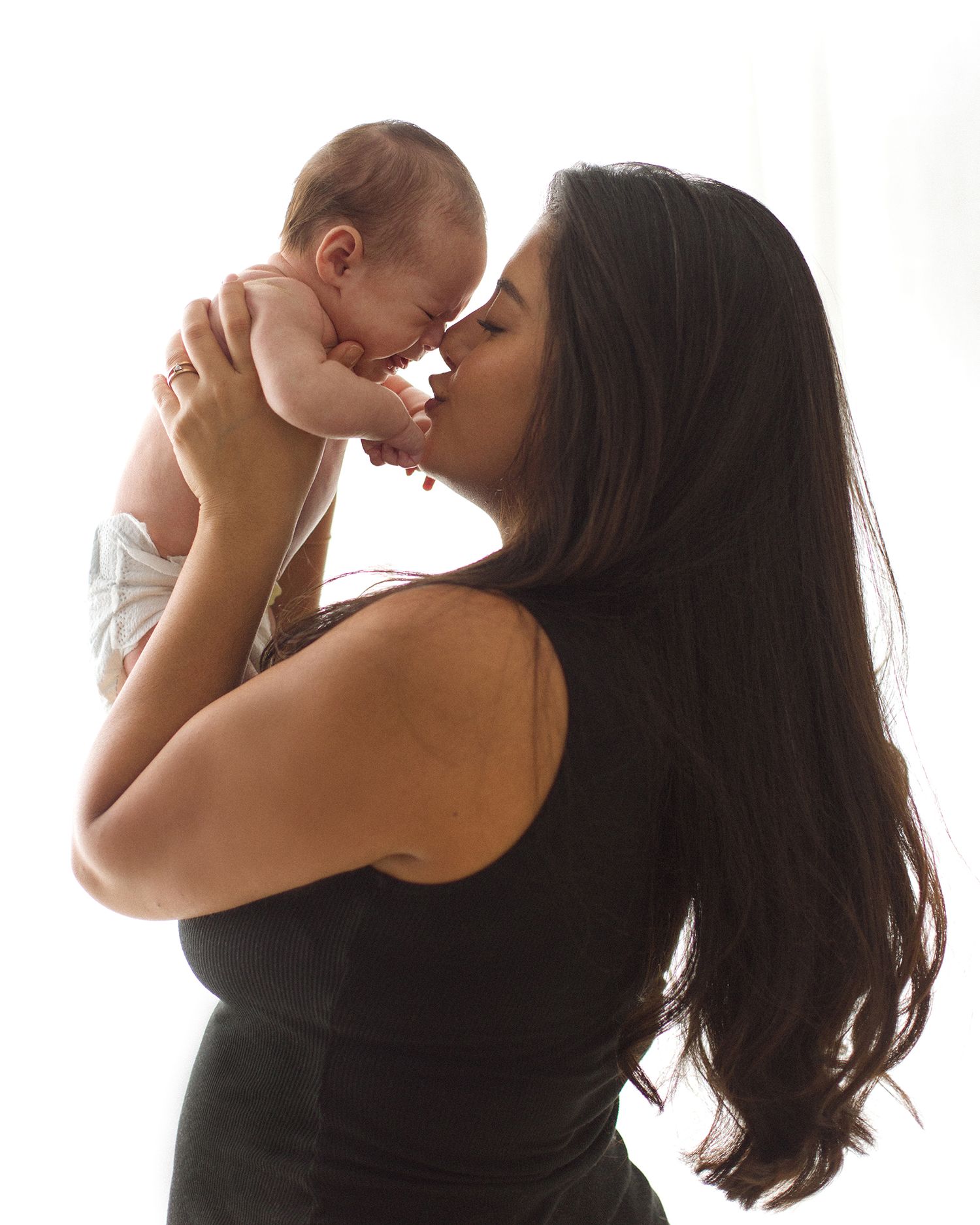 A woman with long dark hair holds a newborn baby up to her face, sharing a tender nose-to-nose moment.