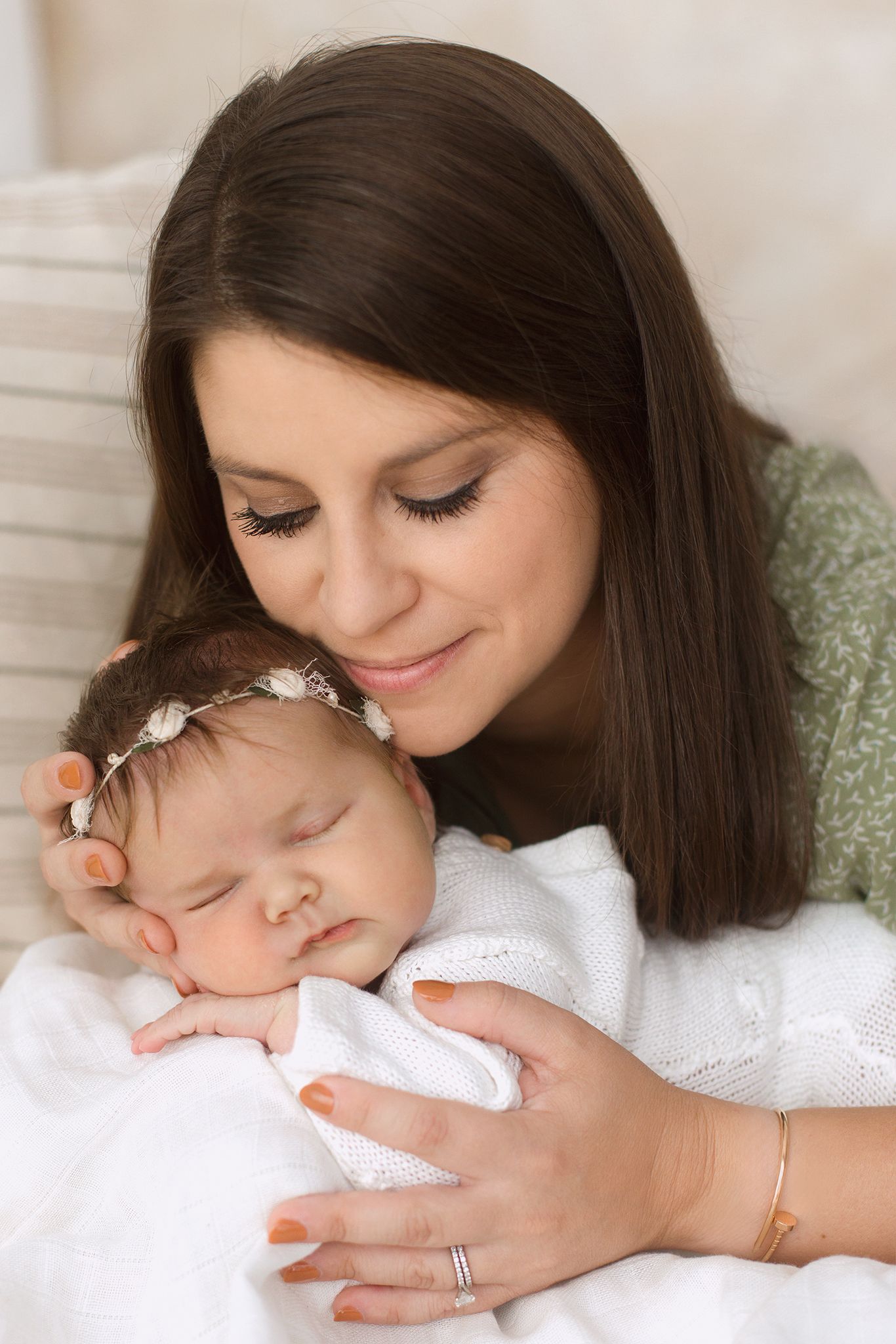 A young mother with dark hair gently cradles her sleeping newborn baby wearing a delicate floral headband.