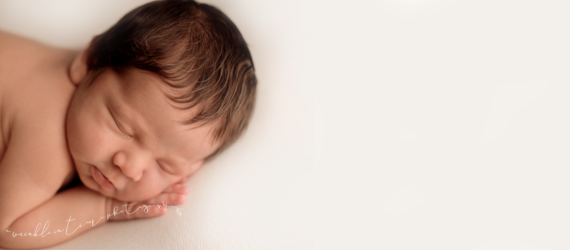 Peaceful sleeping newborn baby with dark hair resting on white background in professional photo.