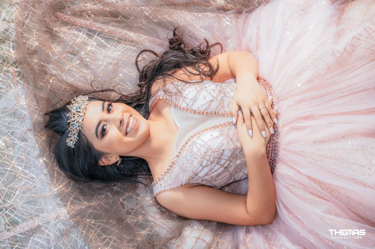 Dreamy bridal portrait of someone lying in a pink tulle gown with a crystal crown against a soft pink backdrop.