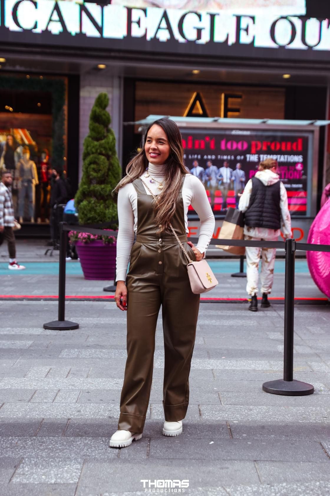 Stylish woman in brown overalls poses outside American Eagle store wearing white sneakers.