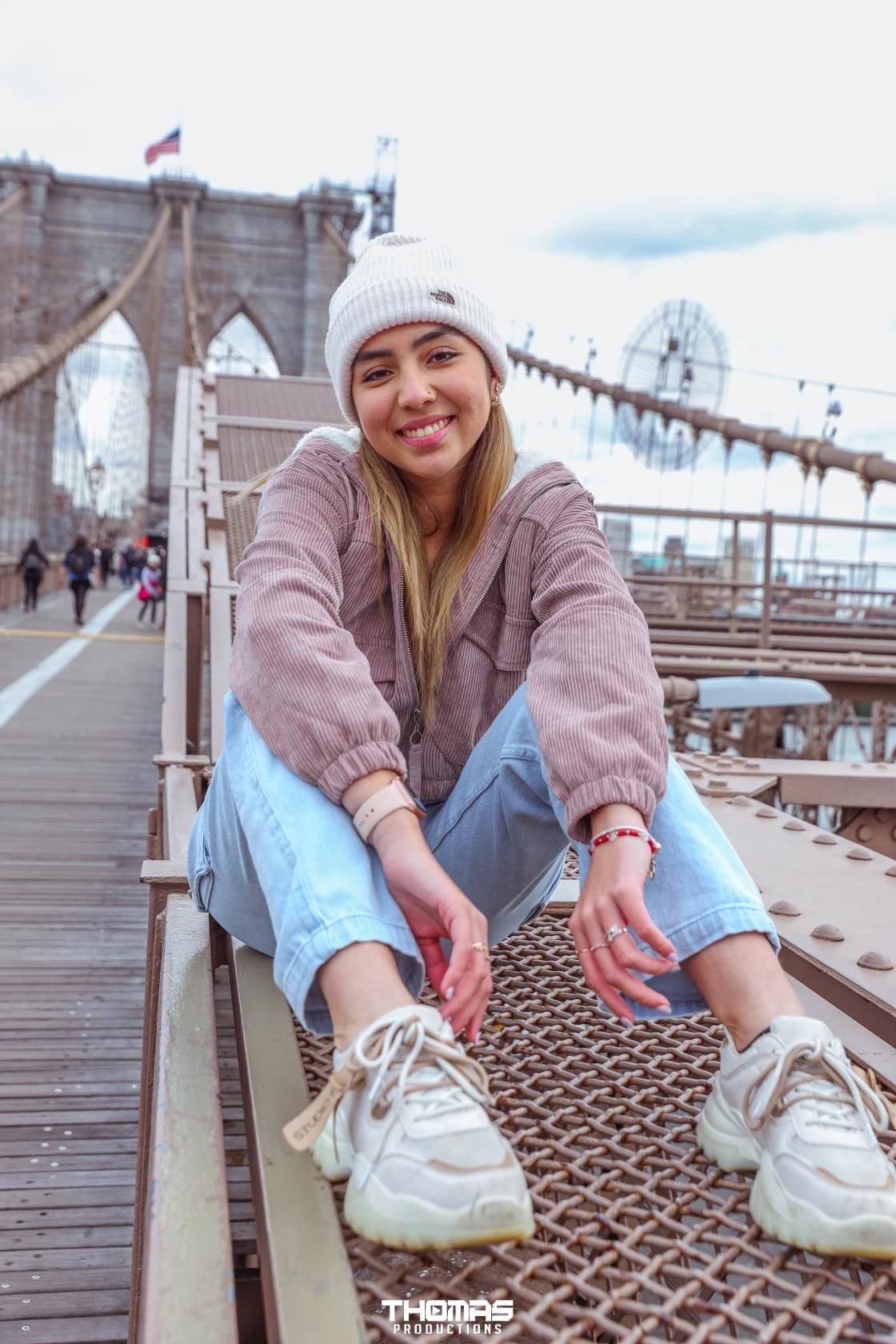 A casual photoshoot on the Brooklyn Bridge walkway with urban architecture in background.