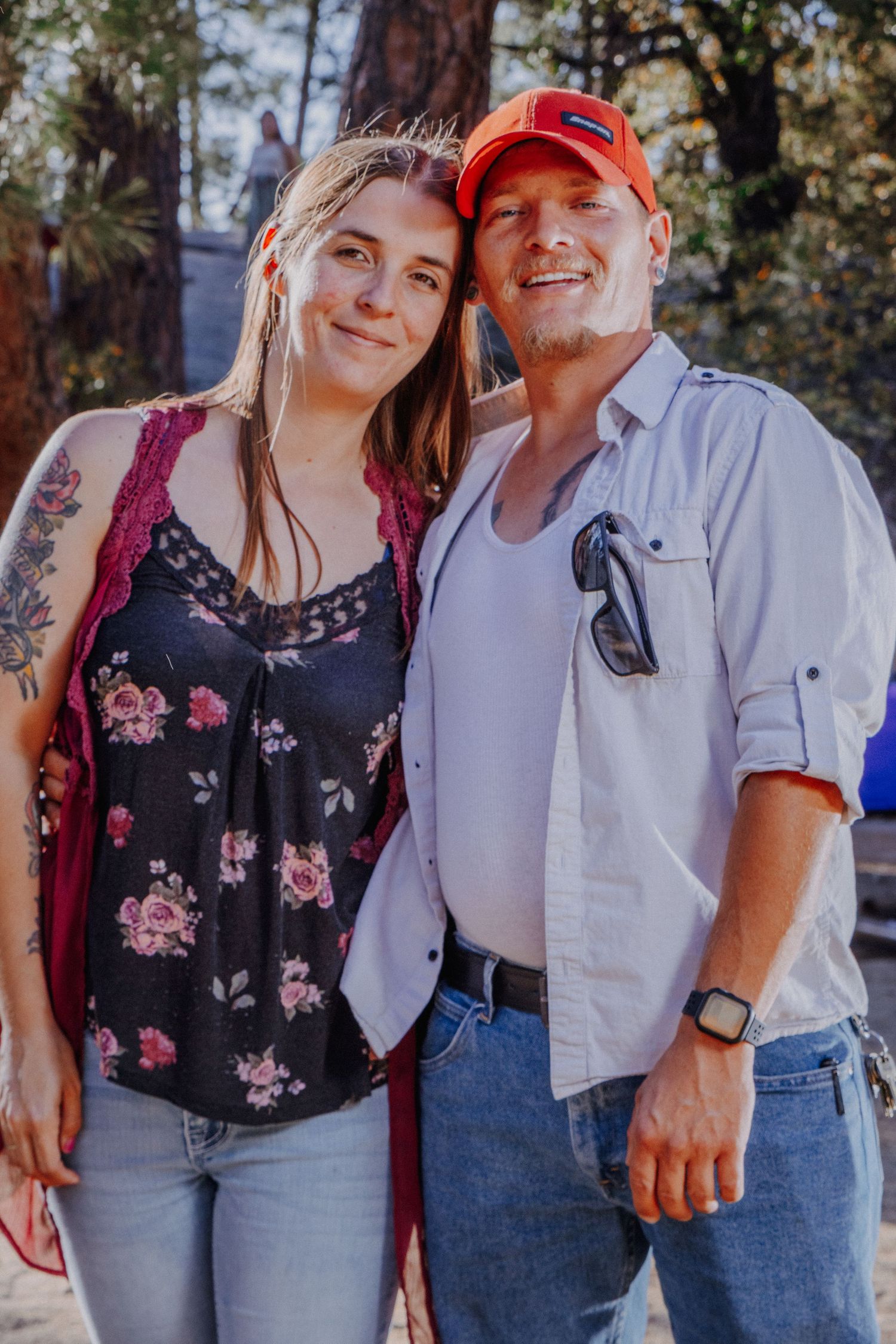 Casual couple in coordinated outfits posing together against forest backdrop.