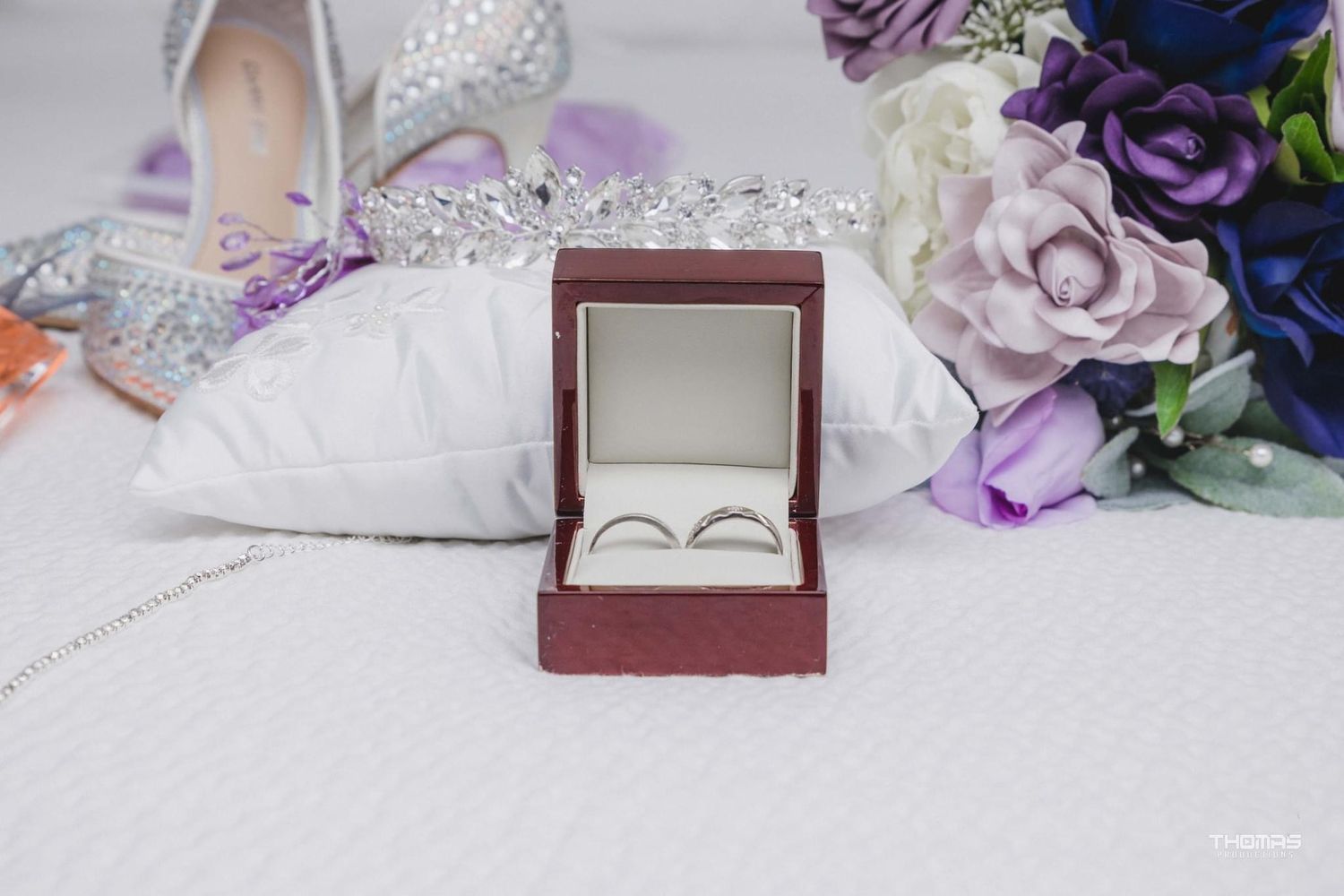 Wedding rings and jewelry displayed on white fabric with purple and blue floral accents.