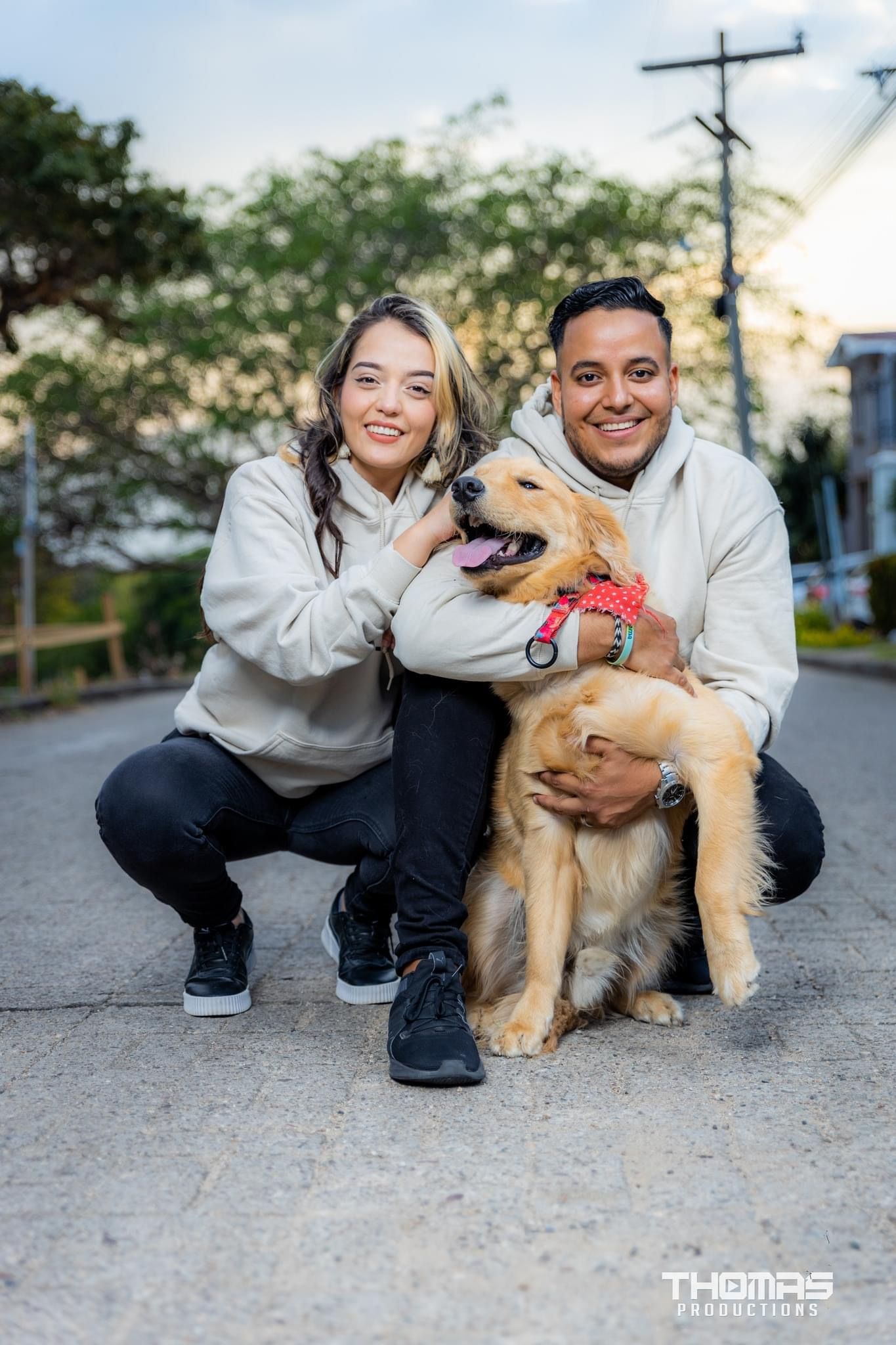 A couple poses with their golden retriever dog on a residential street.