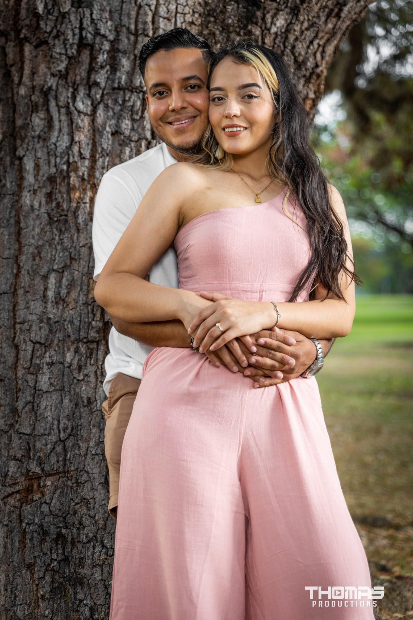 Romantic couple embraces against large tree trunk in outdoor portrait session.