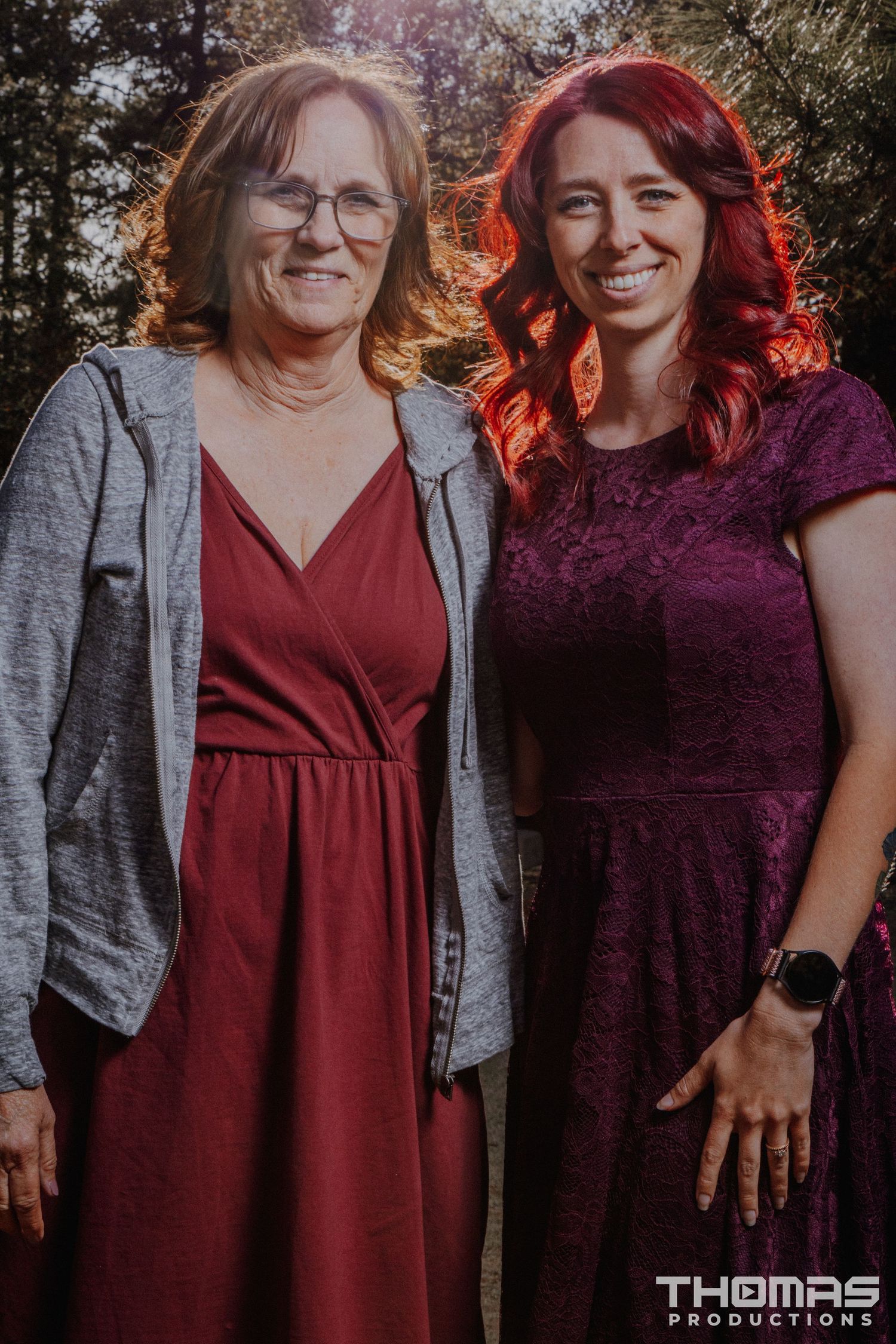 Two people in coordinating red dresses pose together in warm sunset lighting.