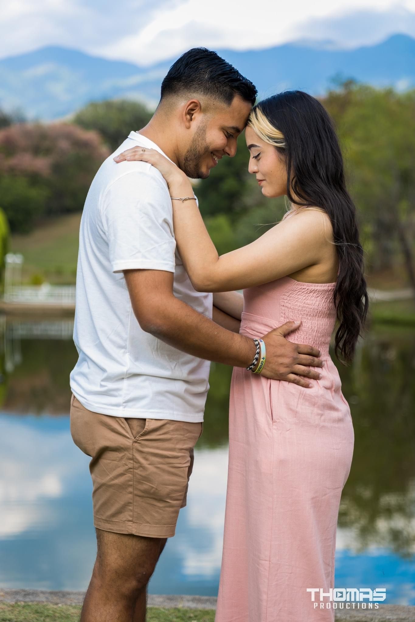 A romantic couple in coordinated outfits embraces by a serene lake during a sunset photoshoot.