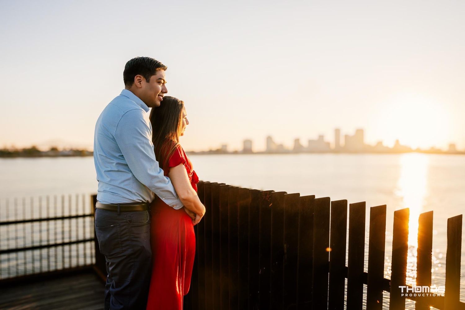 Romantic couple silhouetted against city skyline at sunset on waterfront pier.