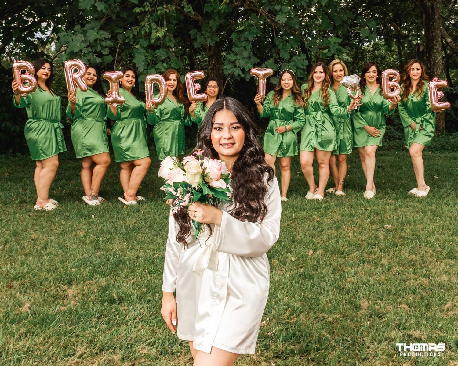 A group wearing green dresses poses on grass for a bridal party photo.