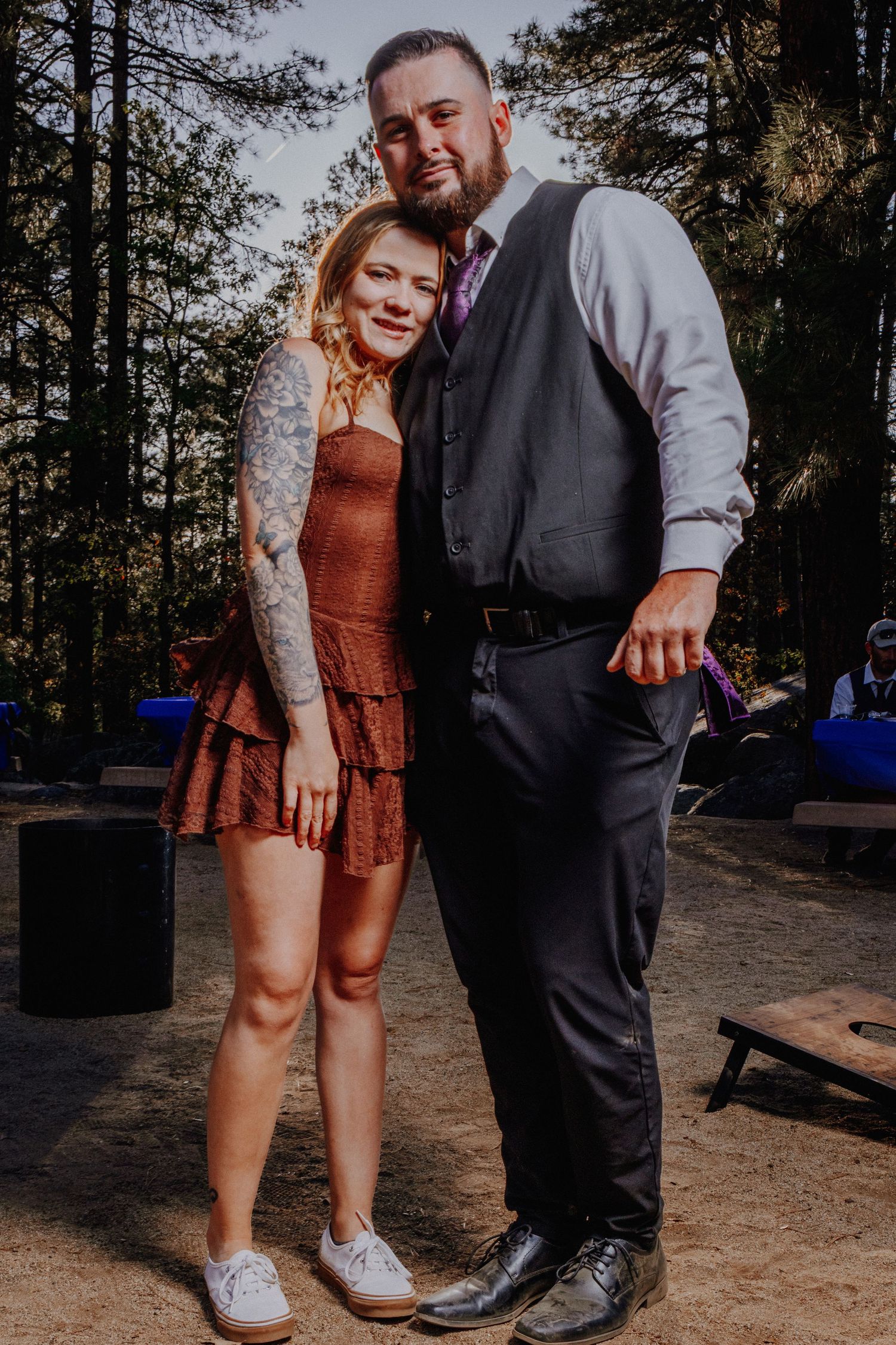Couple posing together in formal wear against natural forest backdrop.