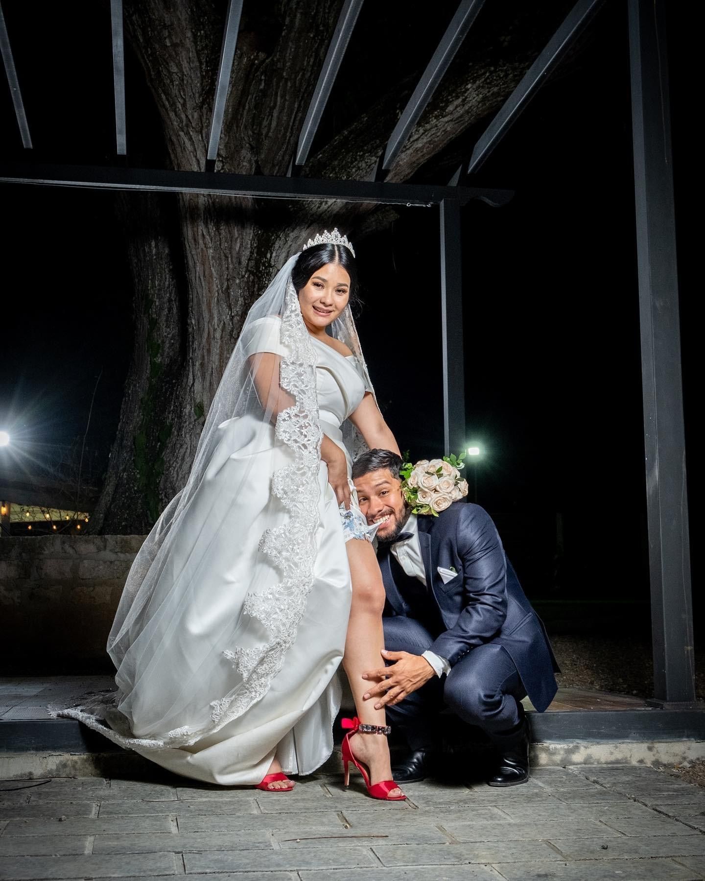 A wedding couple poses dramatically at night, with the bride showing off her red shoes under her lace gown.