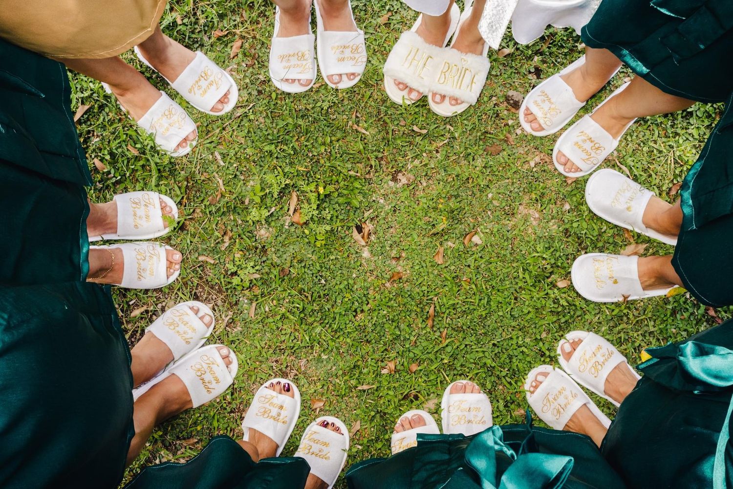 A circle of white sandals arranged on green grass creates a unique wedding detail shot.