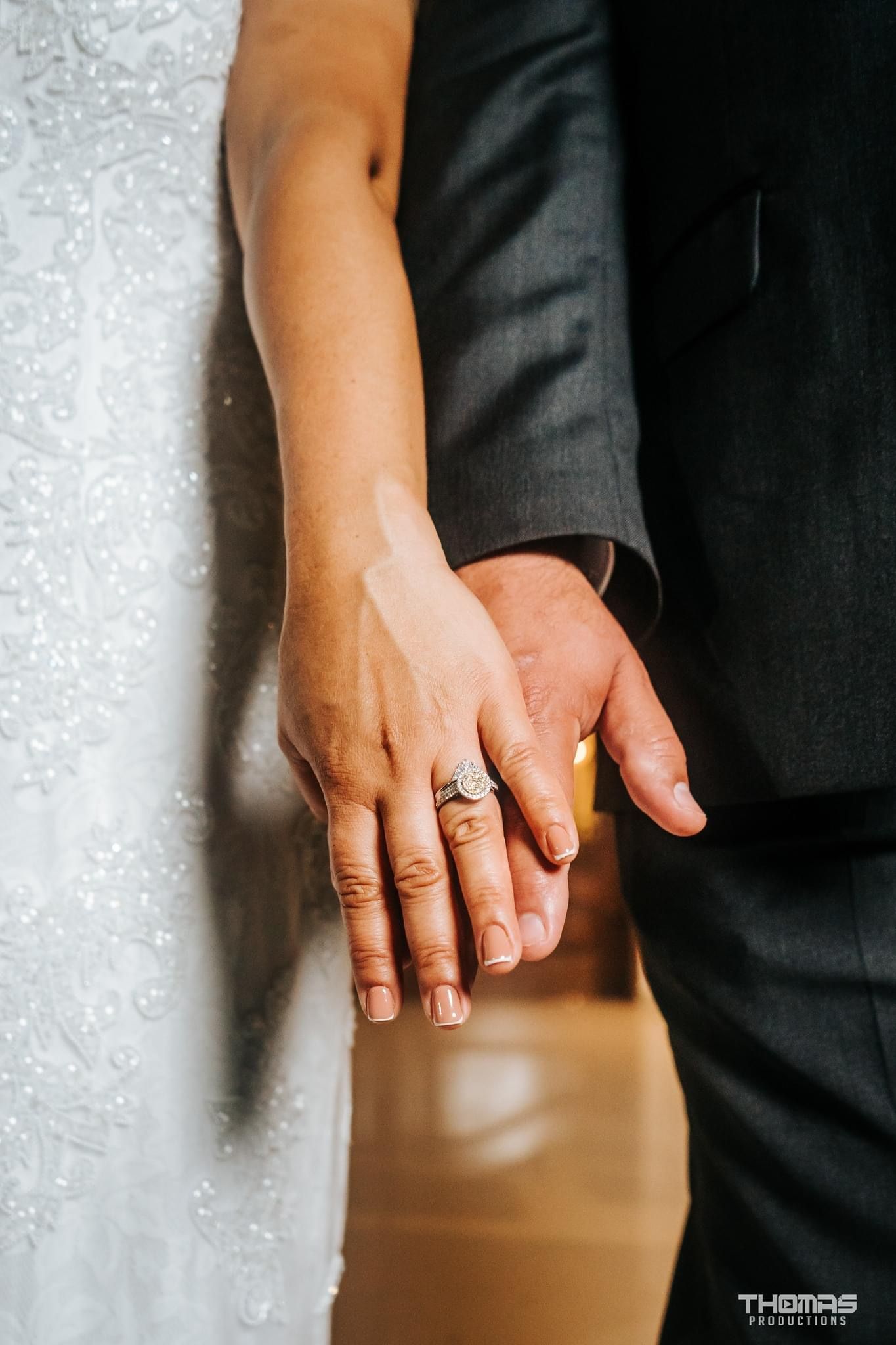 Close-up detail shot of wedding rings on intertwined hands showing black and white attire.